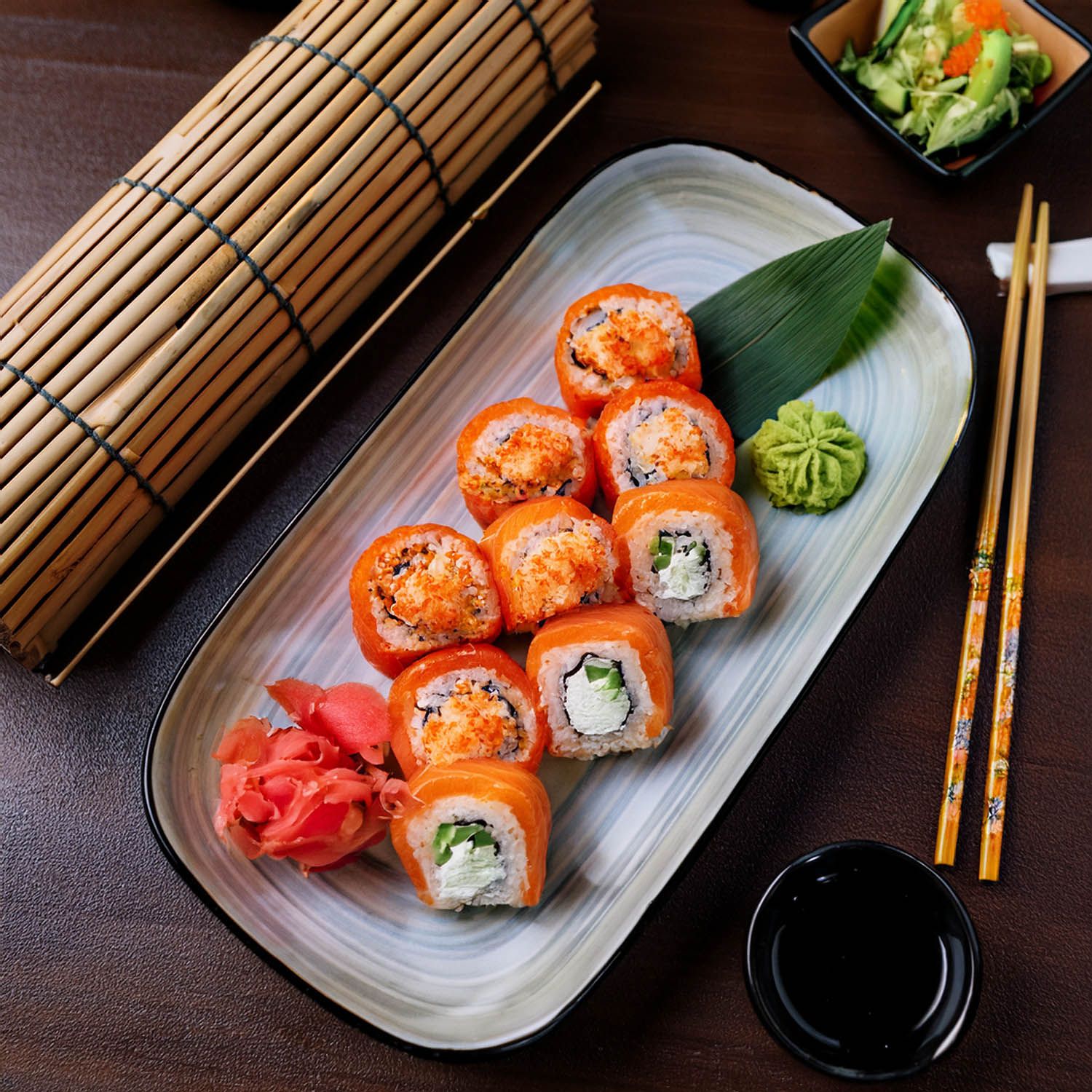Colorati roll di sushi con salmone e verdure serviti su piatti bianchi con una stuoia di bambù.