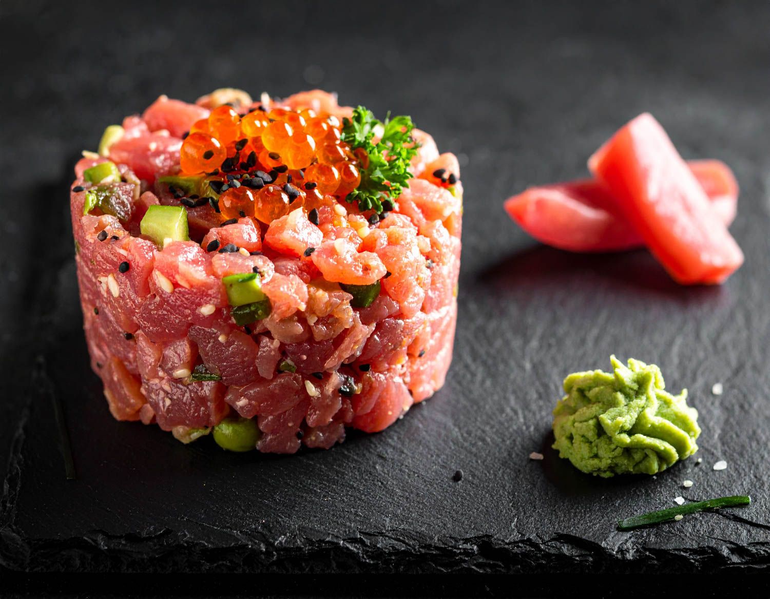 Tartare di tonno crudo con erbe fresche e wasabi servita su piatti di ardesia nera.