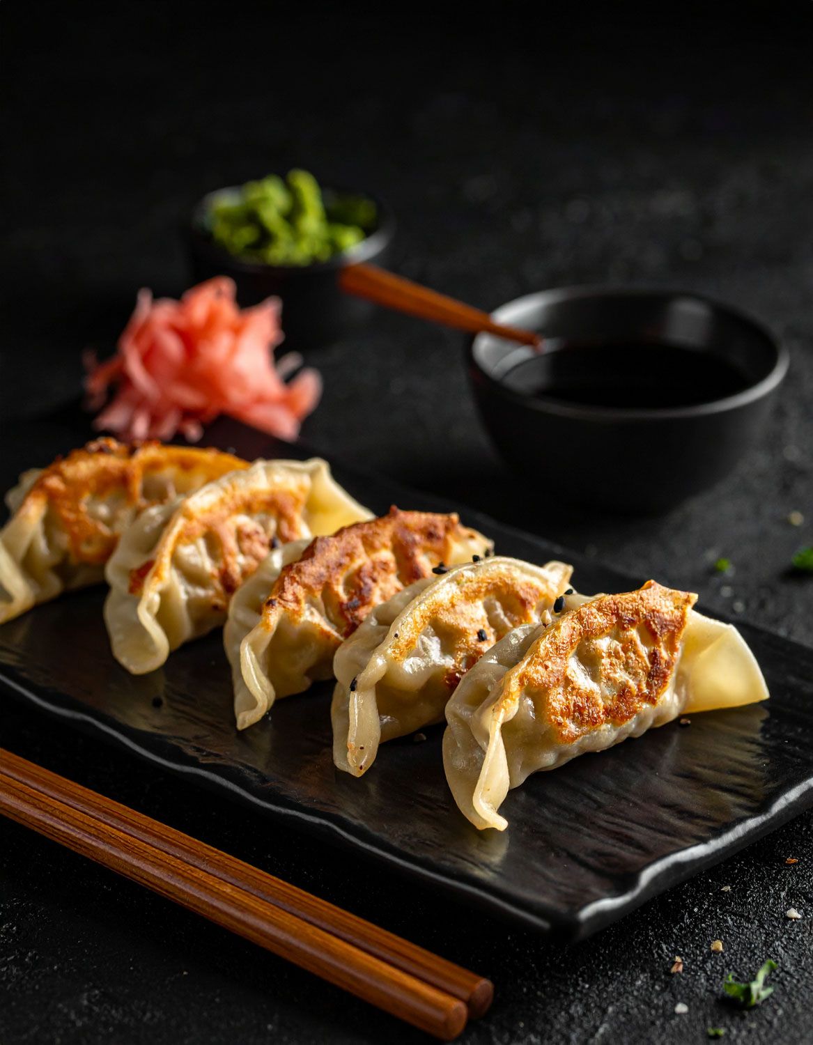Gyoza saltati in padella serviti su un piatto di ardesia nera con salsa da immersione.