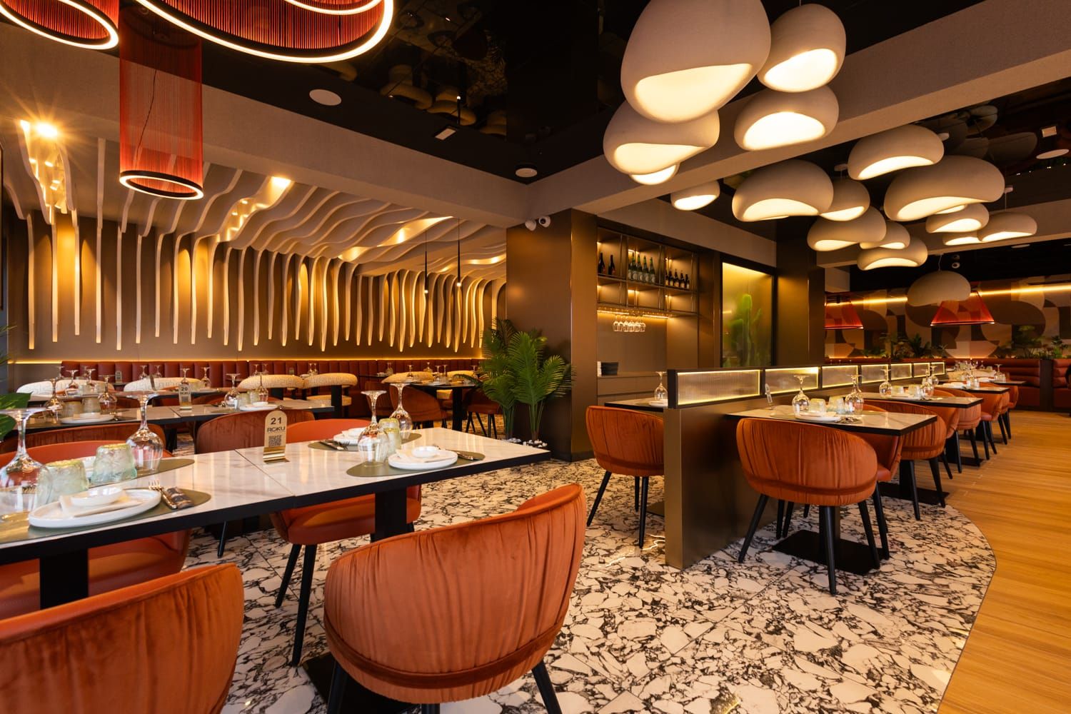 Moderna sala di Roku Sushi Restaurant con divanetti in pelle arancione e lampade a sospensione a Barcellona Pozzo di Gotto.
