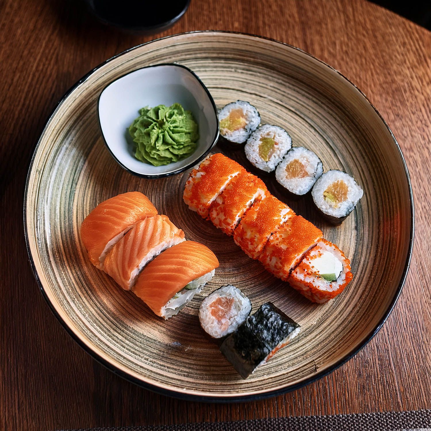 Selezione di sushi tradizionale giapponese con nigiri al salmone e roll su piatti di ceramica rustica.