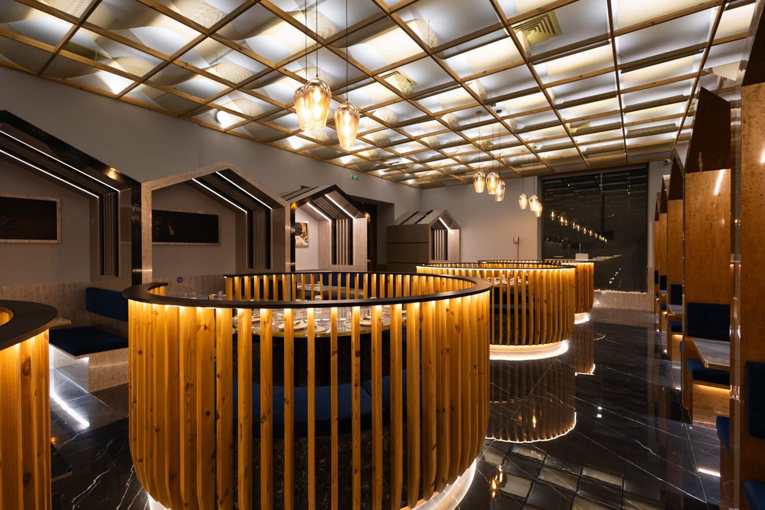 Sala Principale di Roku Sushi Restaurant Trapani, in Sicilia, con la sua parete illuminata da luci calde e tavoli circolari in legno