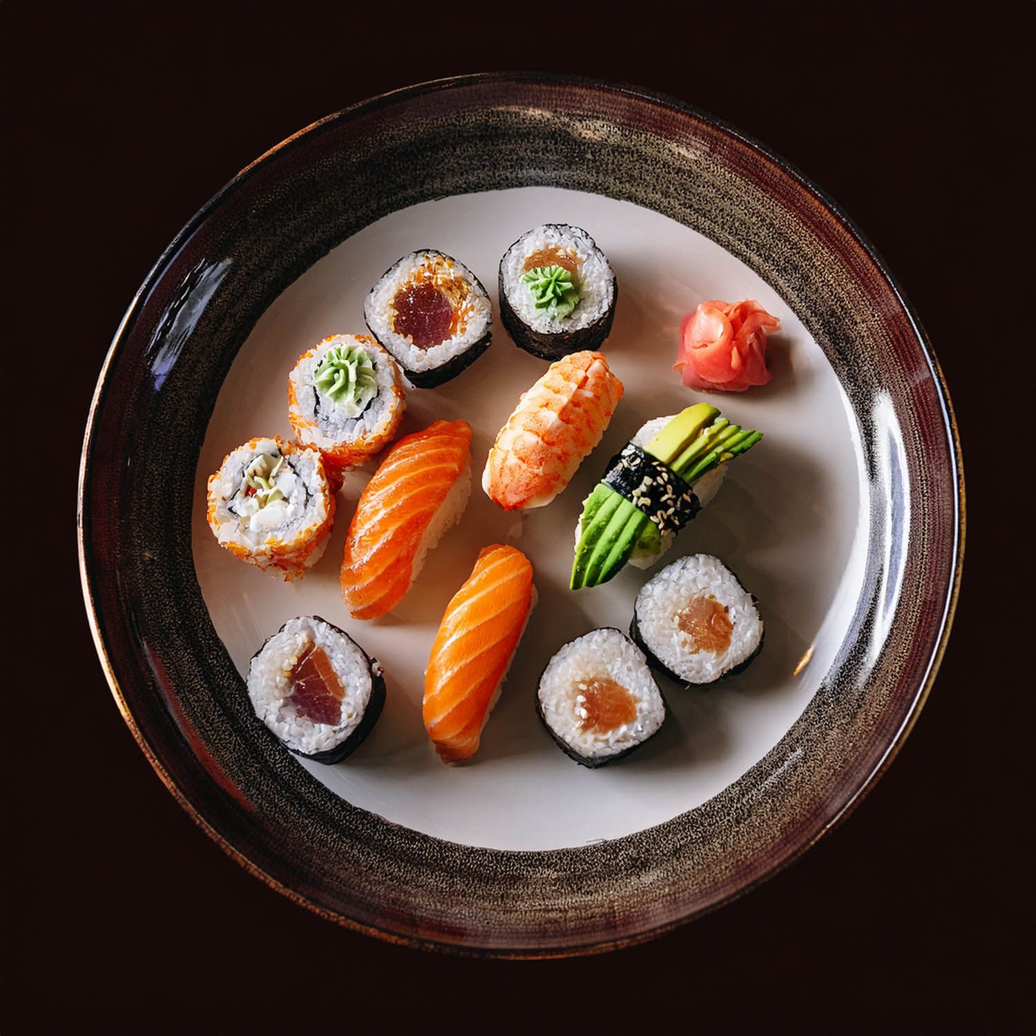 Impiattamento elegante di roll freschi e nigiri su piatti ovali in ceramica con bordi scuri.