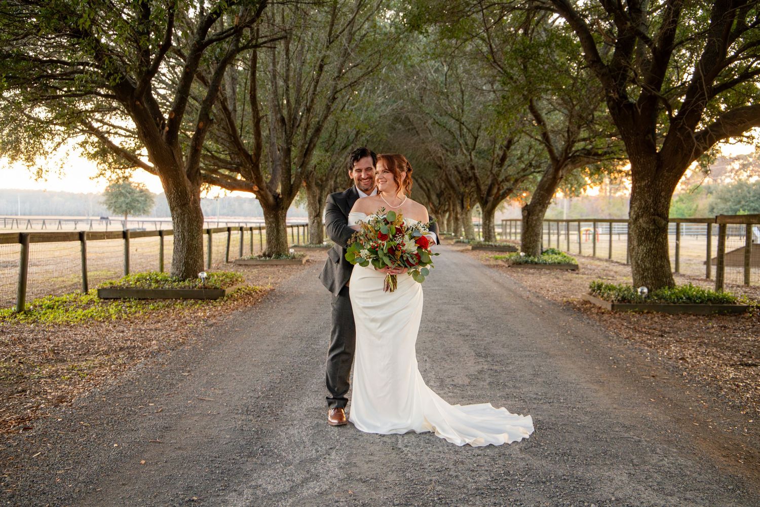 A couple walks along a tree-lined path in a romantic outdoor setting during a wedding photo session.