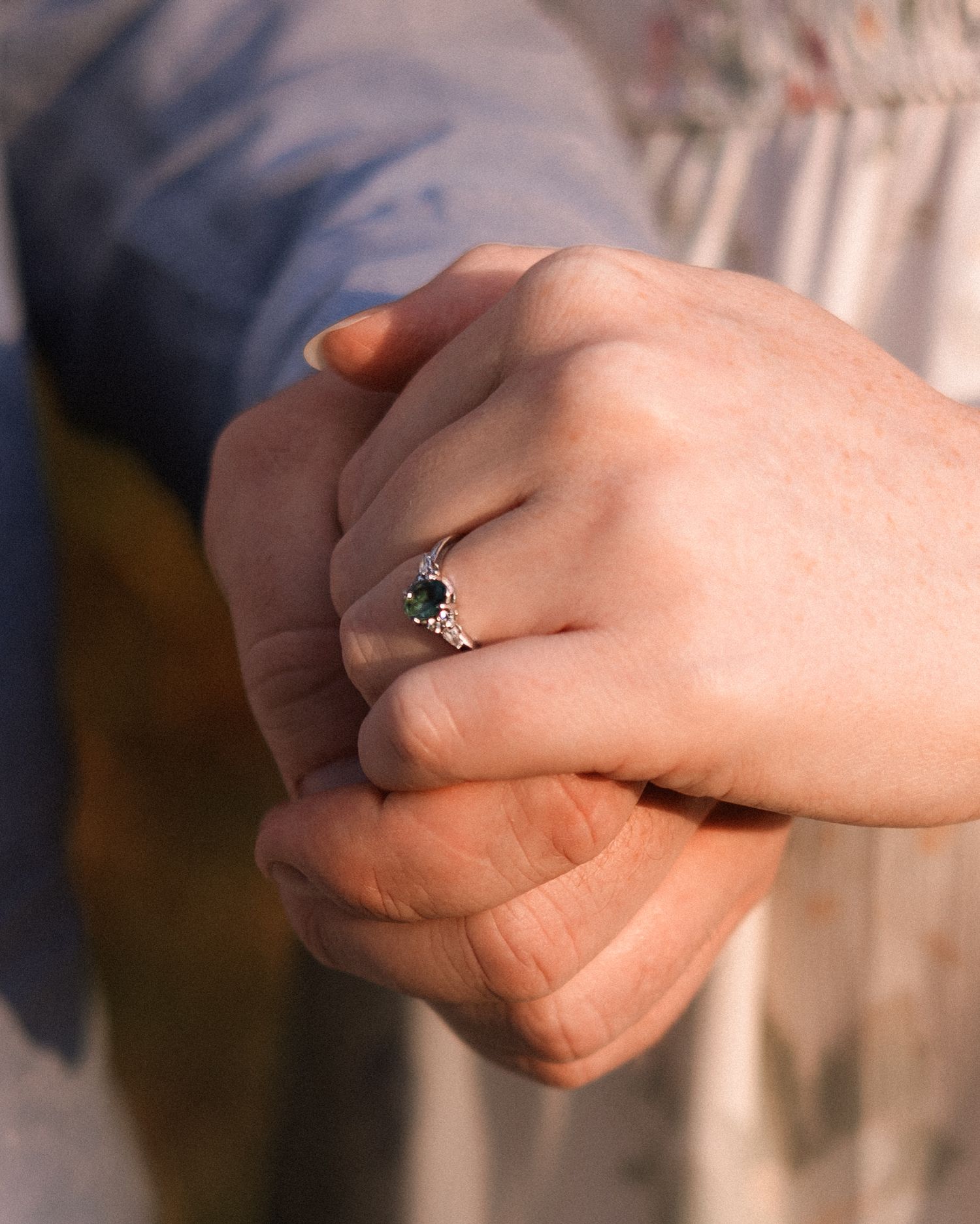 Close-up of hands holding with a silver engagement ring featuring a green gemstone.