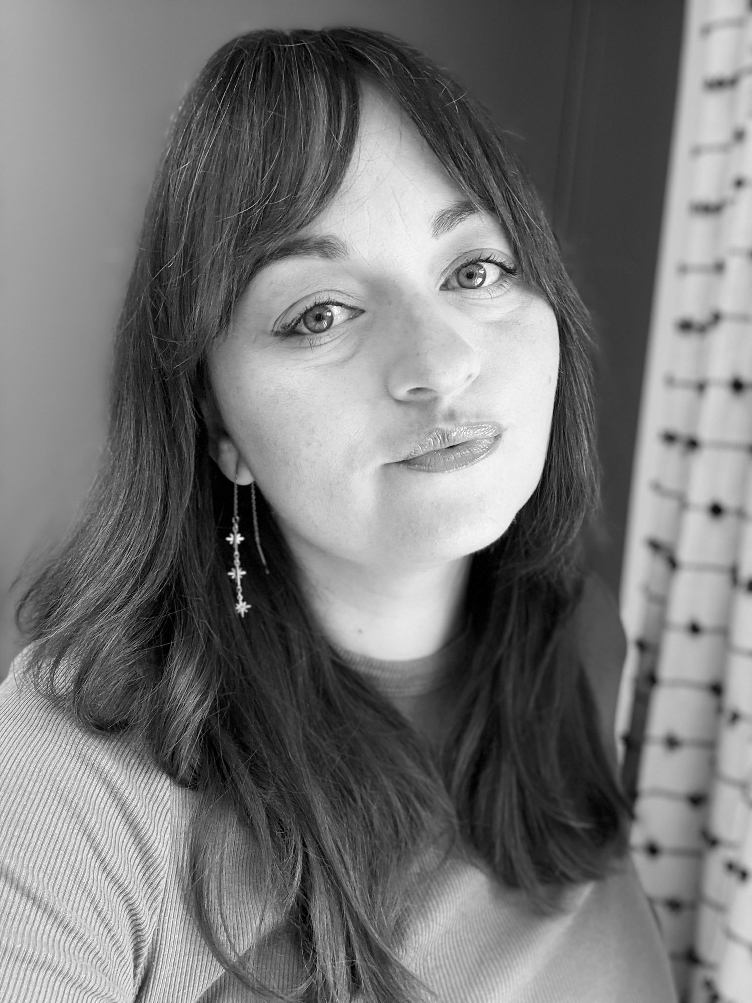 Black and white close-up portrait of a young woman with long hair, bangs, and dangling earrings.