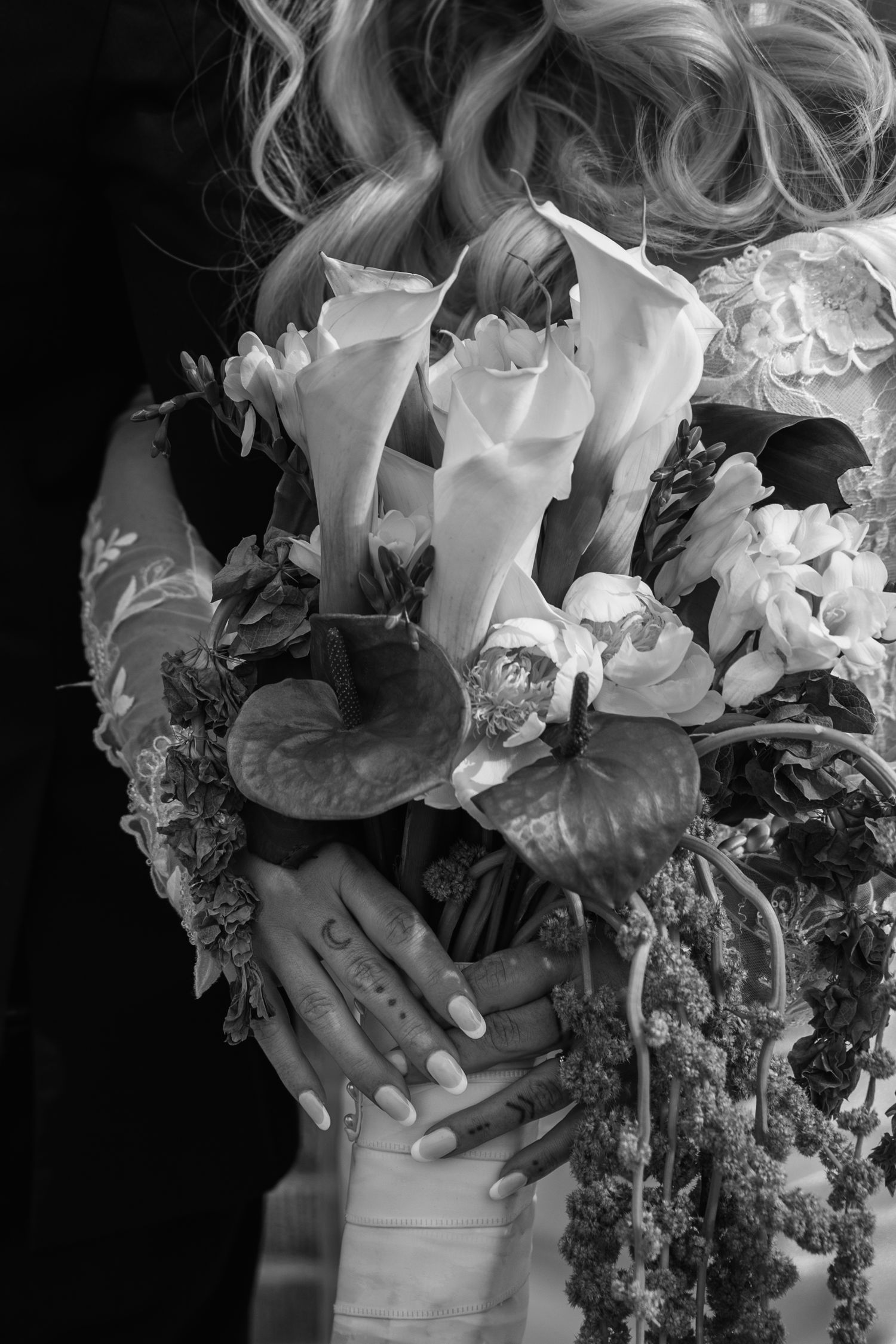 Bride holding an elegant wedding bouquet of calla lilies and tropical flowers, black and white photo.