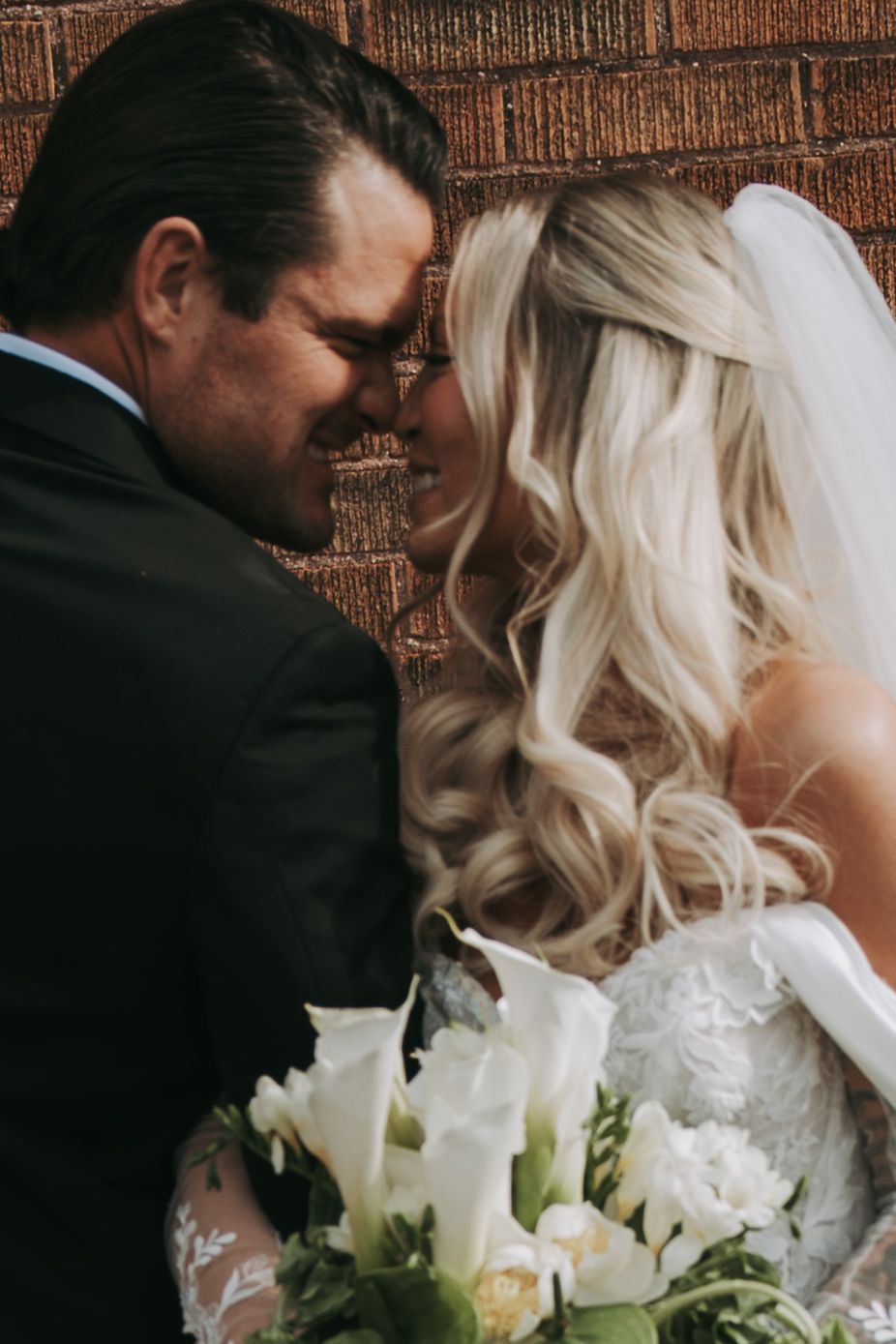 Bride and groom share a romantic forehead touch while holding white calla lily bouquet.