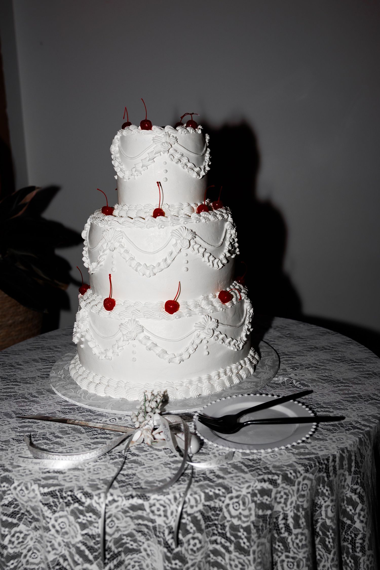 Elegant three-tier white wedding cake decorated with red cherries on a lace tablecloth.