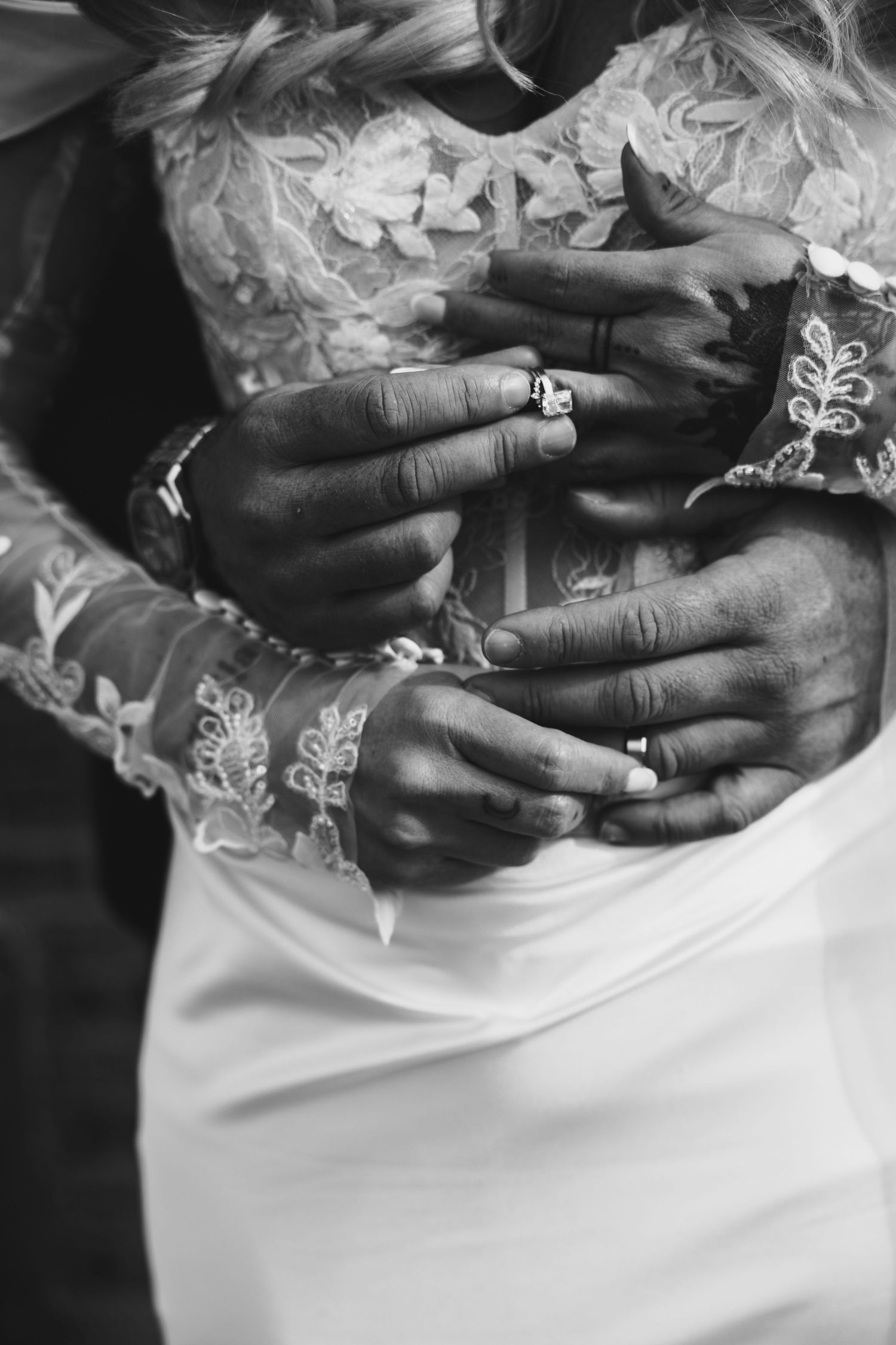 Close-up black and white photo of newlyweds hands with wedding rings in lace wedding dress.