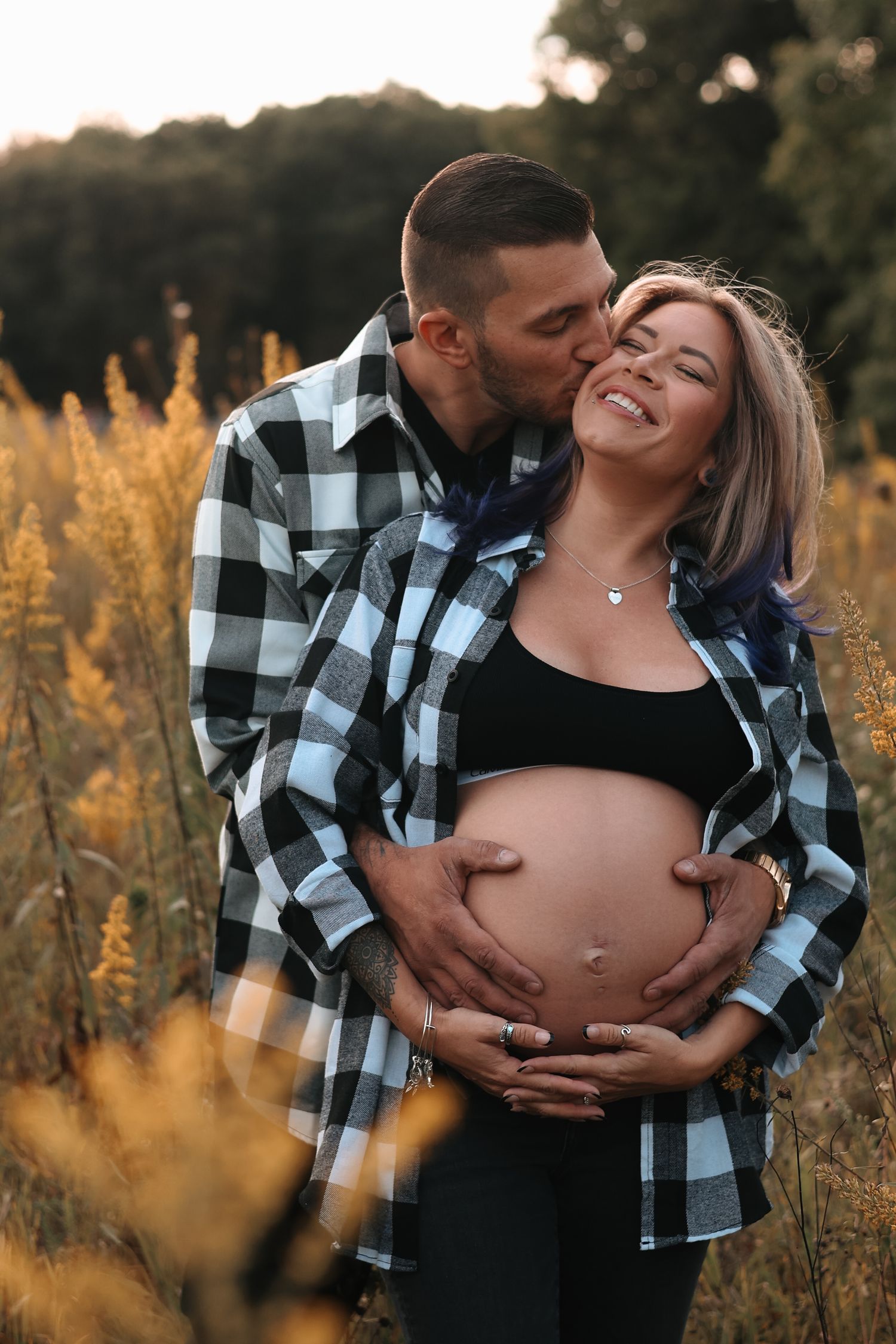 Man kissing smiling pregnant woman in a golden field during a warm sunset maternity shoot.