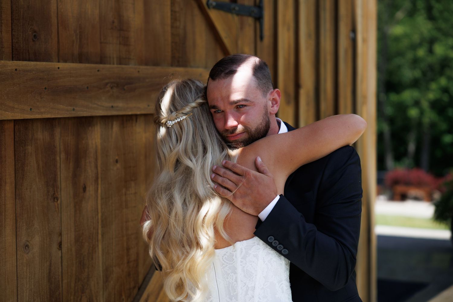Bride and groom share an emotional first look hug outside a rustic wooden barn on their wedding day.