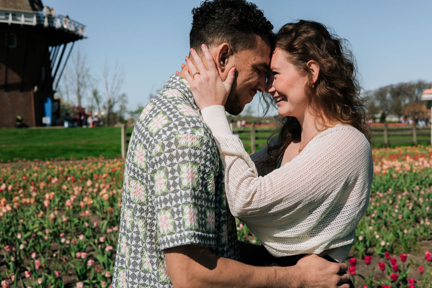 Happy couple embracing forehead to forehead in a vibrant tulip field with a windmill visible in the background.