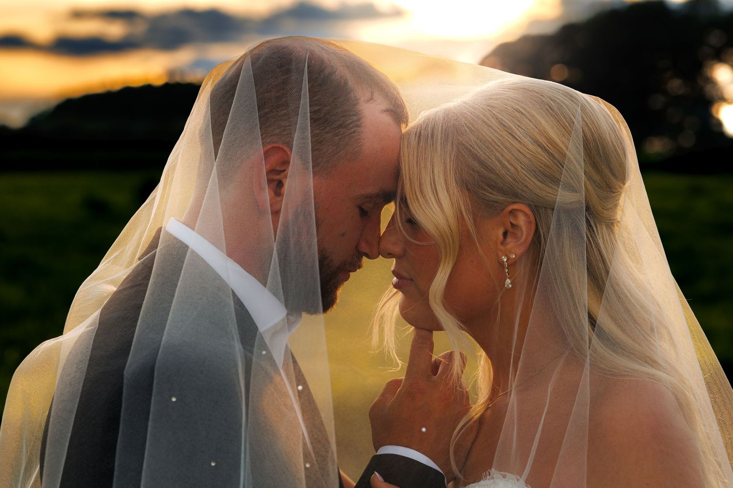 Bride and groom share an intimate moment under a veil at golden hour sunset.