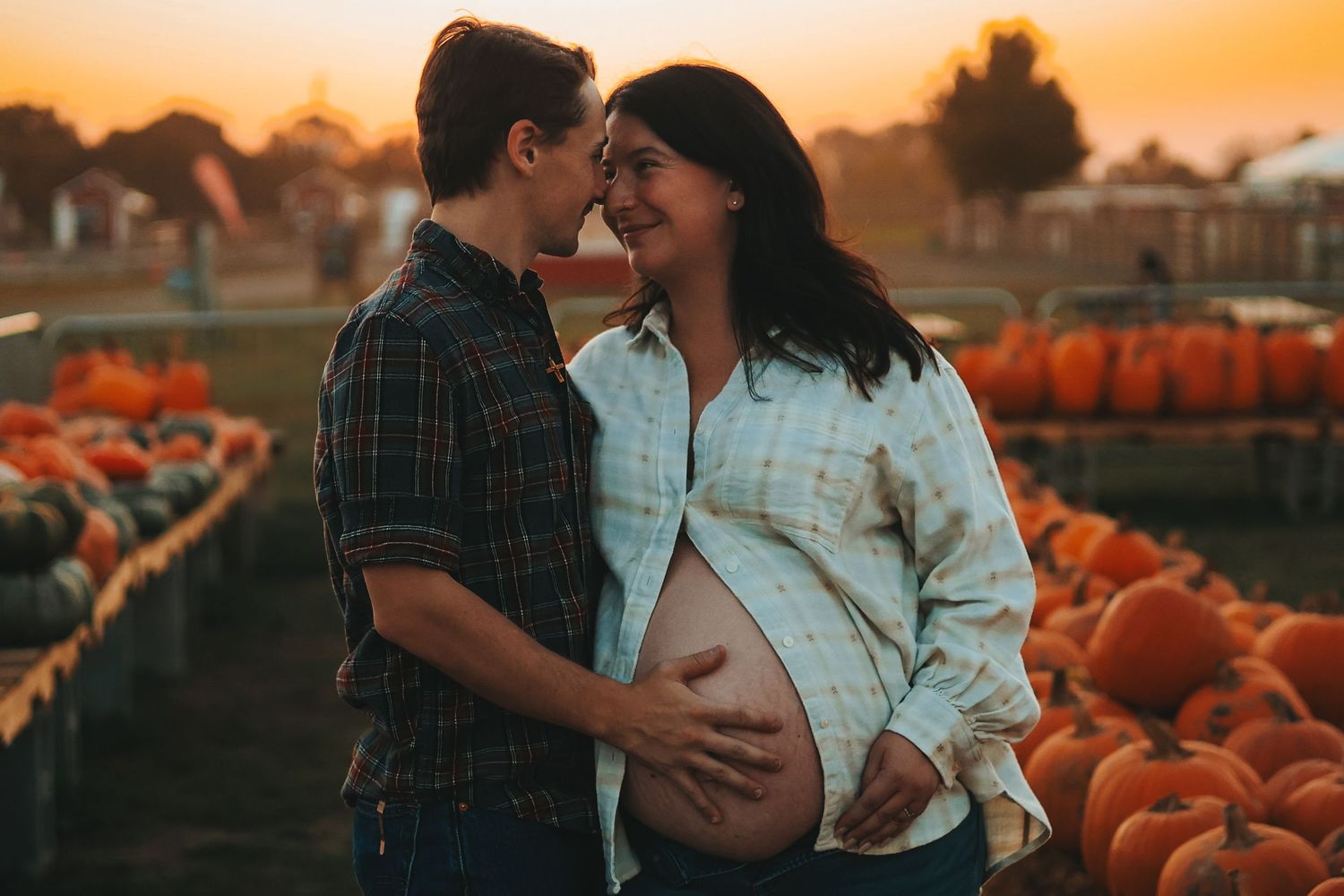 A couple shares a romantic moment at a pumpkin patch during a golden sunset maternity photo session.