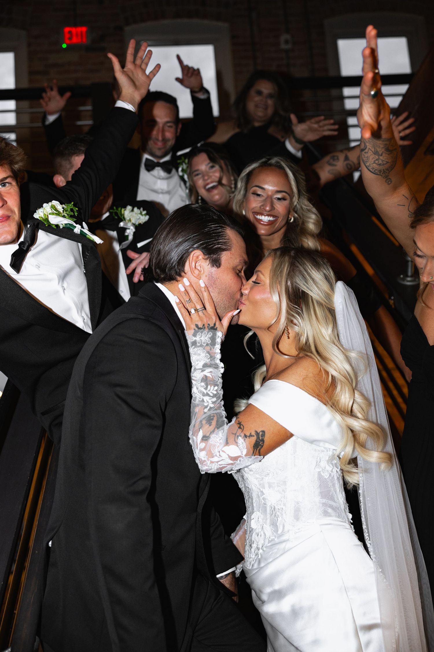 Bride and groom share a passionate kiss surrounded by cheering wedding guests.