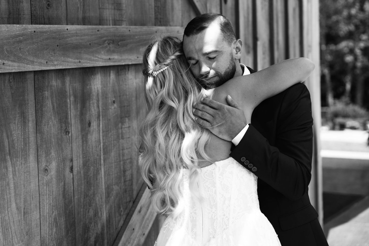 Emotional black and white photo of bride and groom sharing a tender embrace during first look at barn venue.