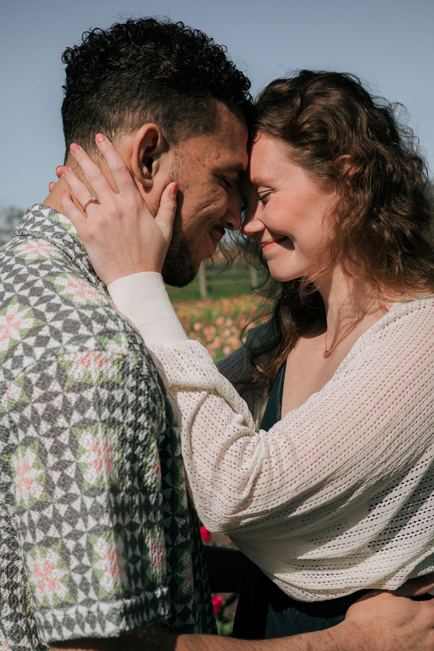 Happy engaged couple touching foreheads and smiling in a sunny tulip garden setting.
