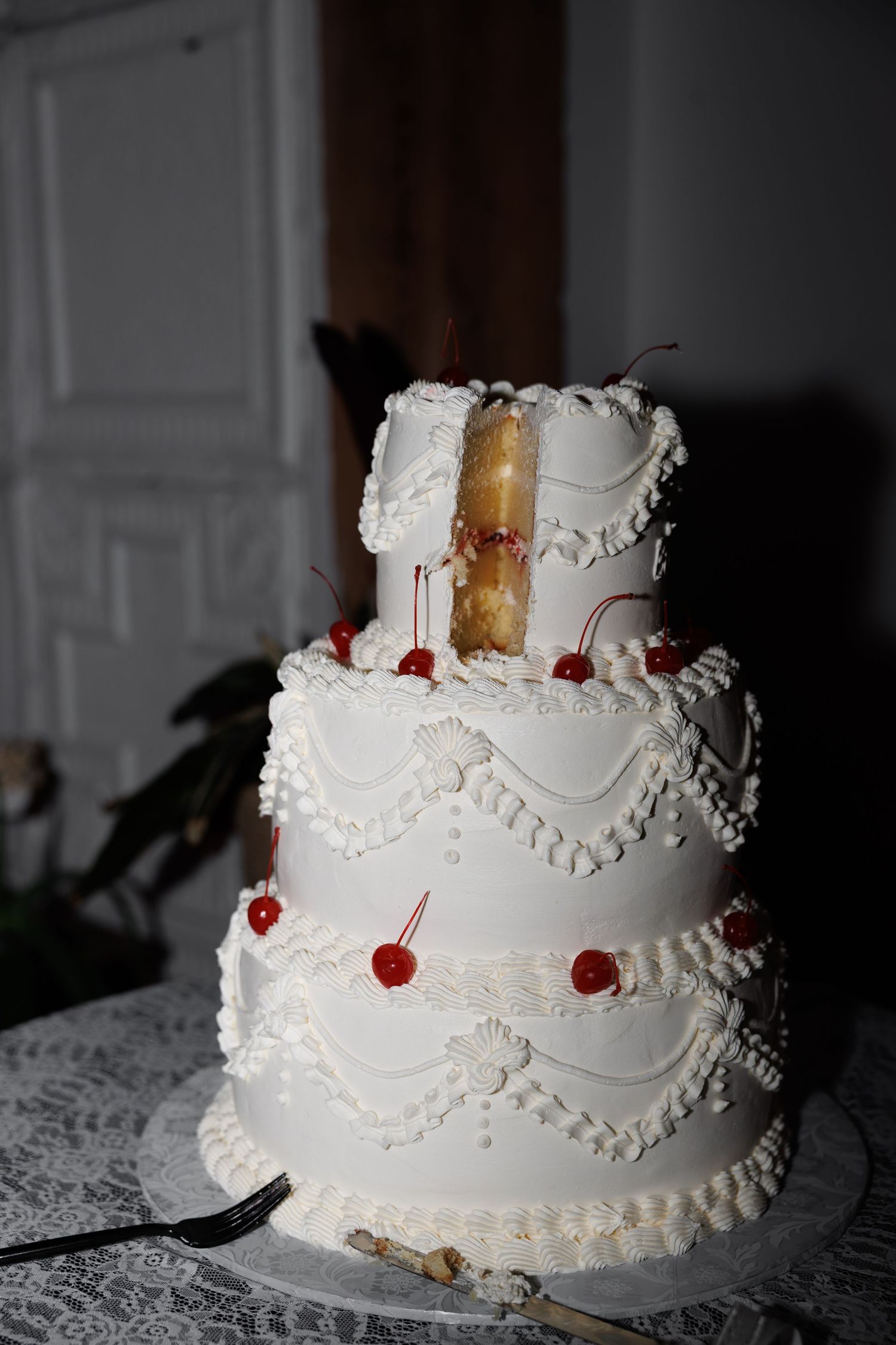 Three-tier white wedding cake decorated with red cherries and intricate piped frosting details.