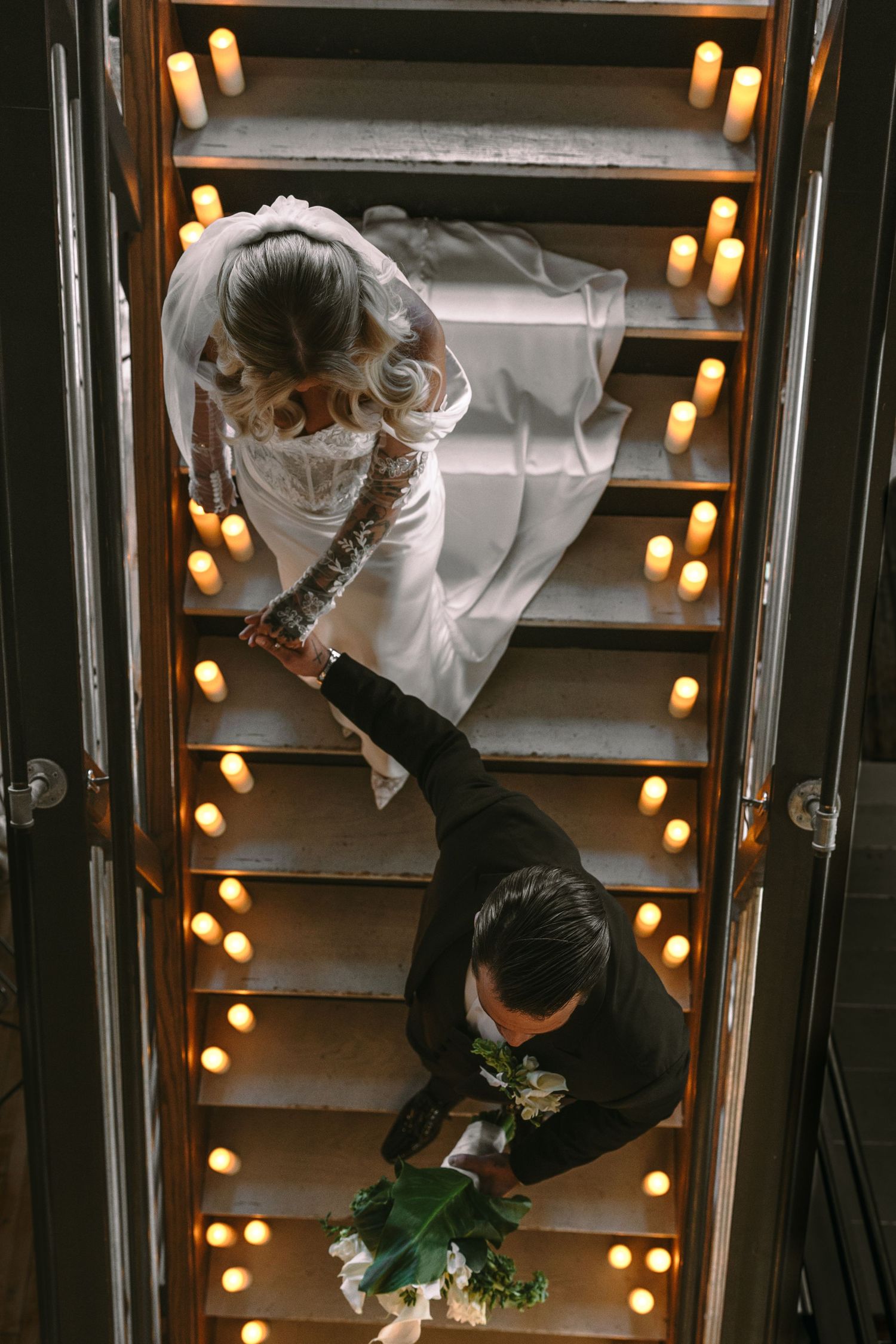 Aerial view of bride and groom descending candlelit staircase at elegant wedding venue.