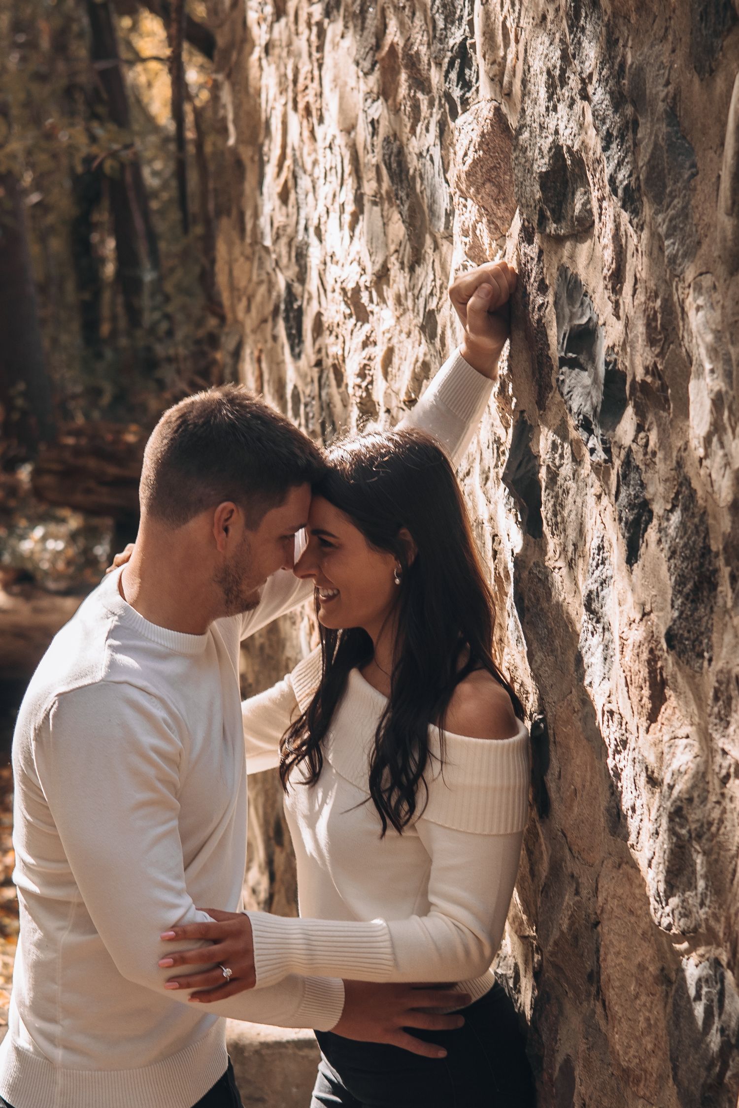 Romantic couple leaning close together against a rustic stone wall in an intimate outdoor setting.