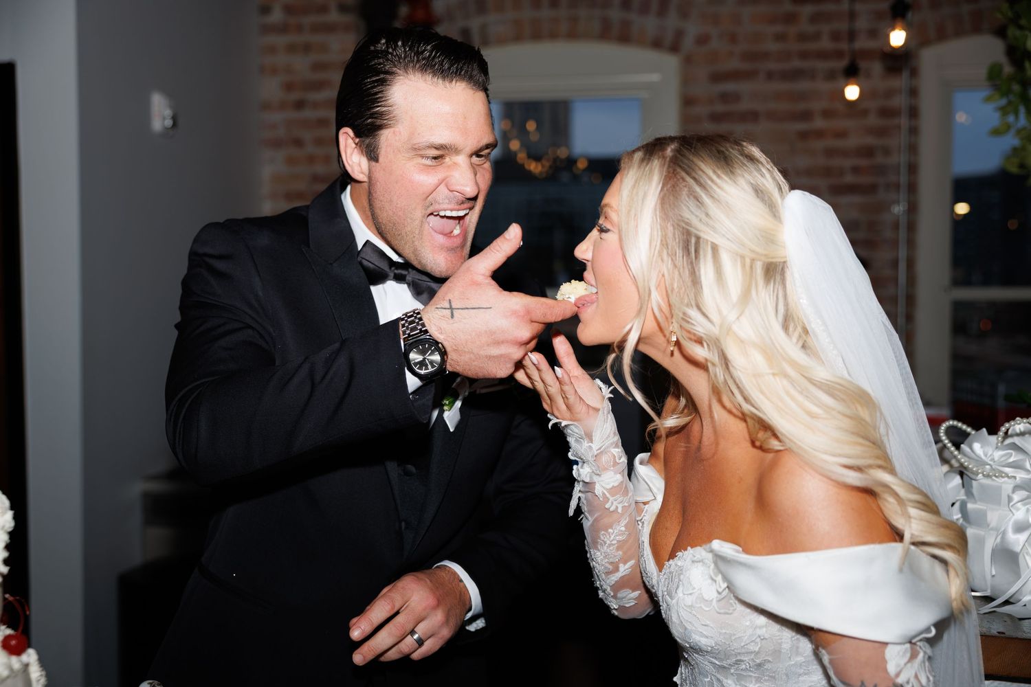 Groom feeds wedding cake to laughing bride in a fun candid reception moment.