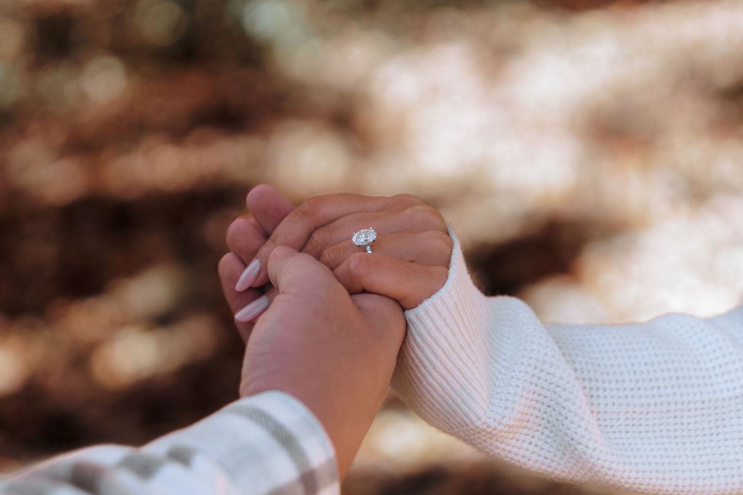 Close-up of two hands holding gently with a diamond solitaire engagement ring visible.