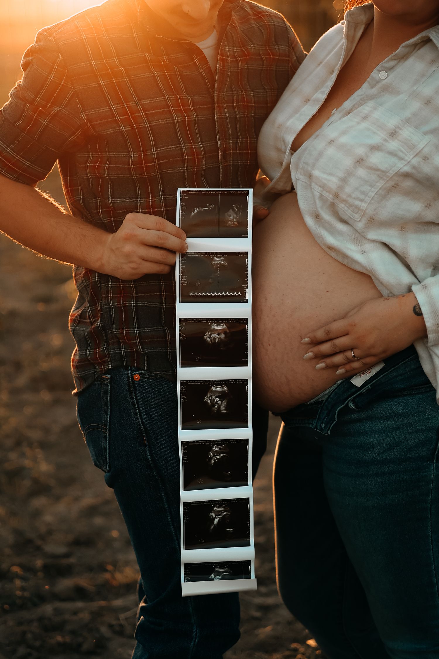 A couple displays a strip of ultrasound images beside a pregnant belly during a sunset maternity shoot.