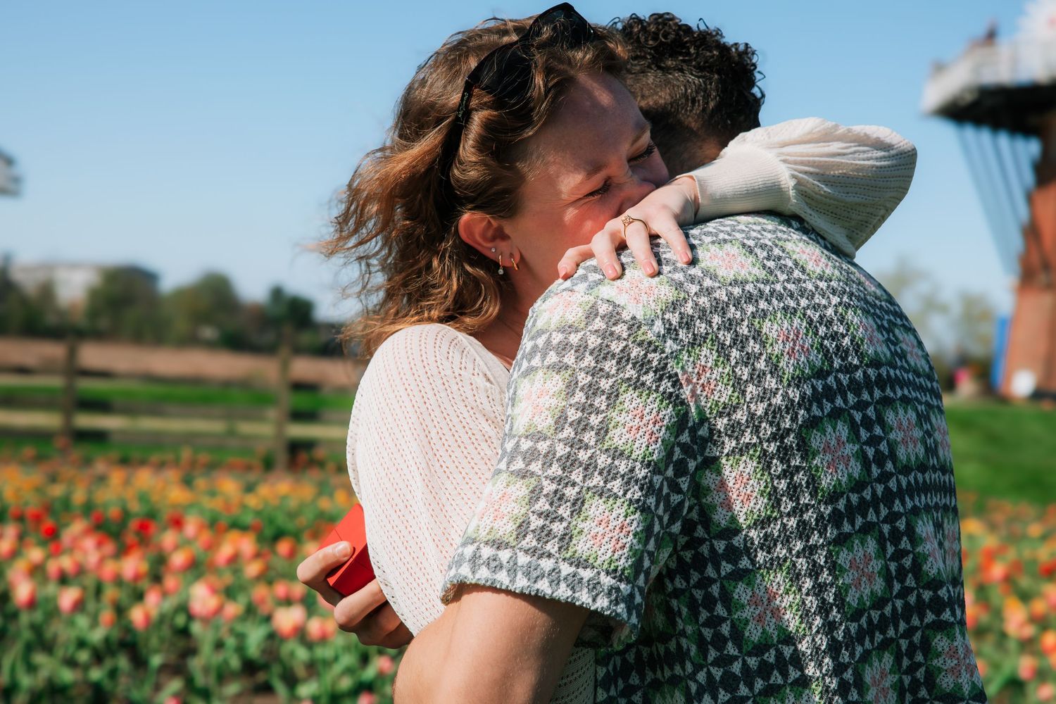 Couple embracing and hugging in front of a colorful tulip field on a sunny day.