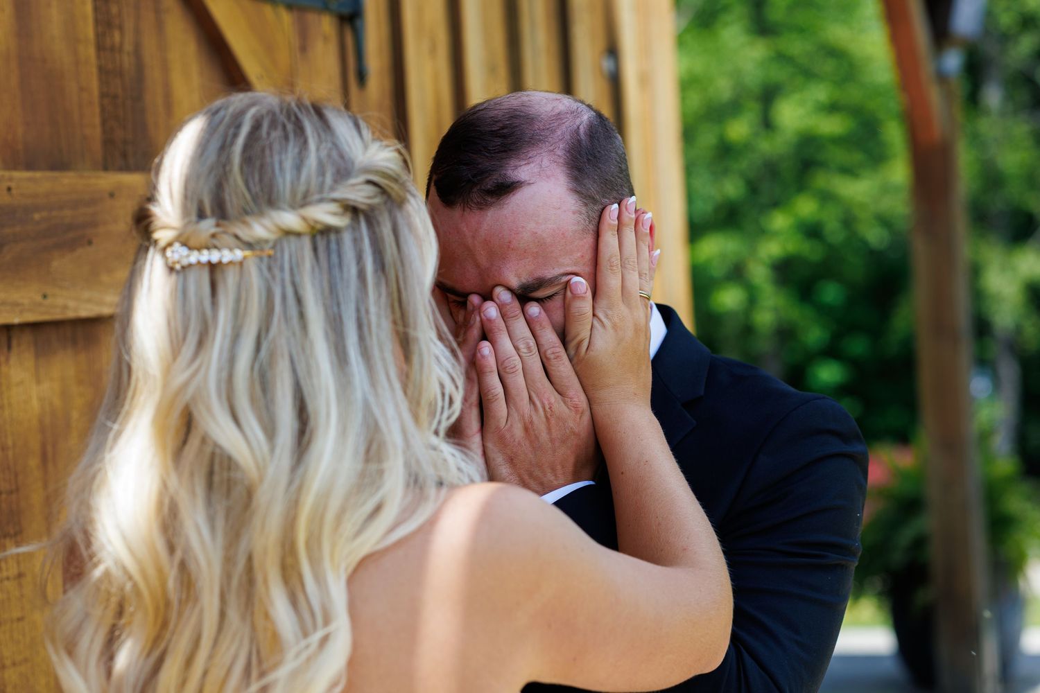 Emotional groom covering his face with hands in tears during wedding first look moment with blonde bride.
