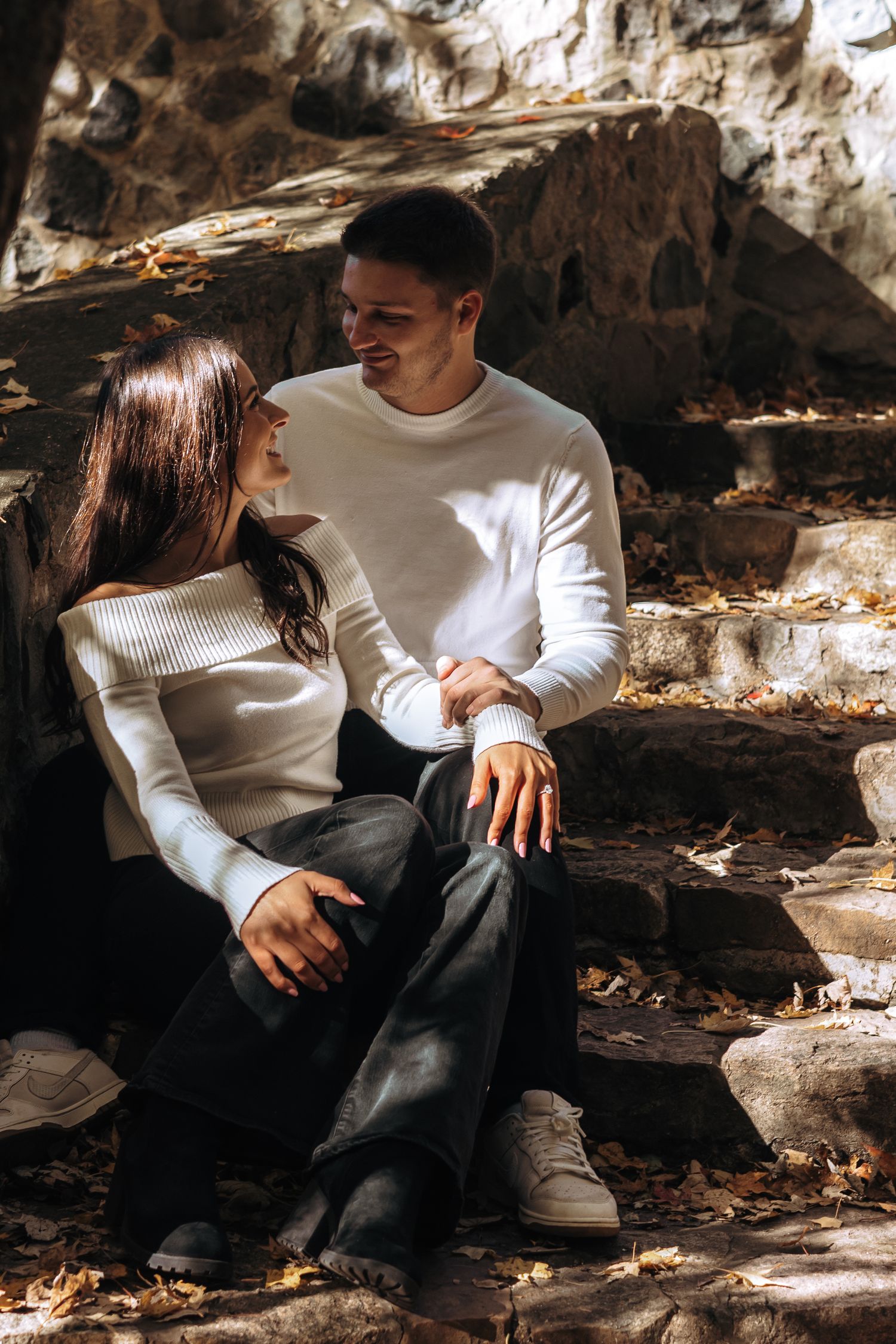 Couple in white sweaters sitting together on stone steps in dappled autumn sunlight.