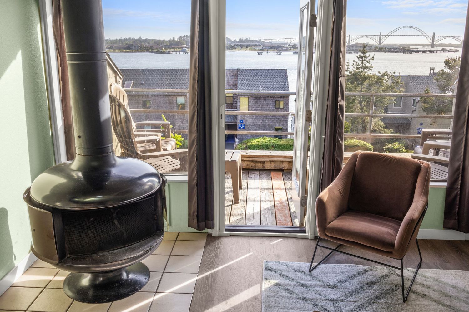 View from coastal apartment living area with black pot-belly stove and open balcony doors overlooking Yaquina Bay and bridge in Newport, OR