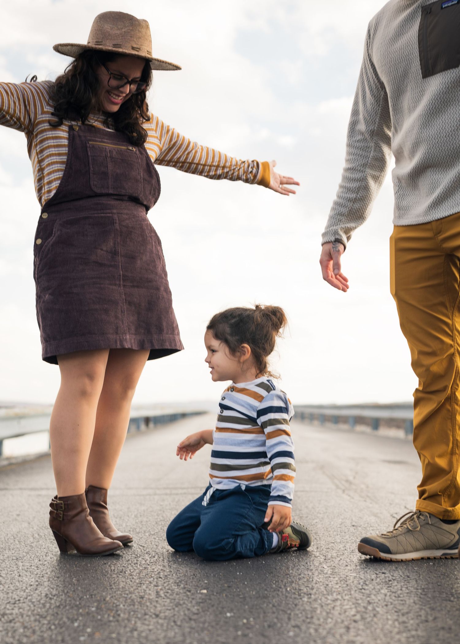 A young child sits on a road while two adults reach down toward them on a cloudy day outdoors in Chattanooga, TN.