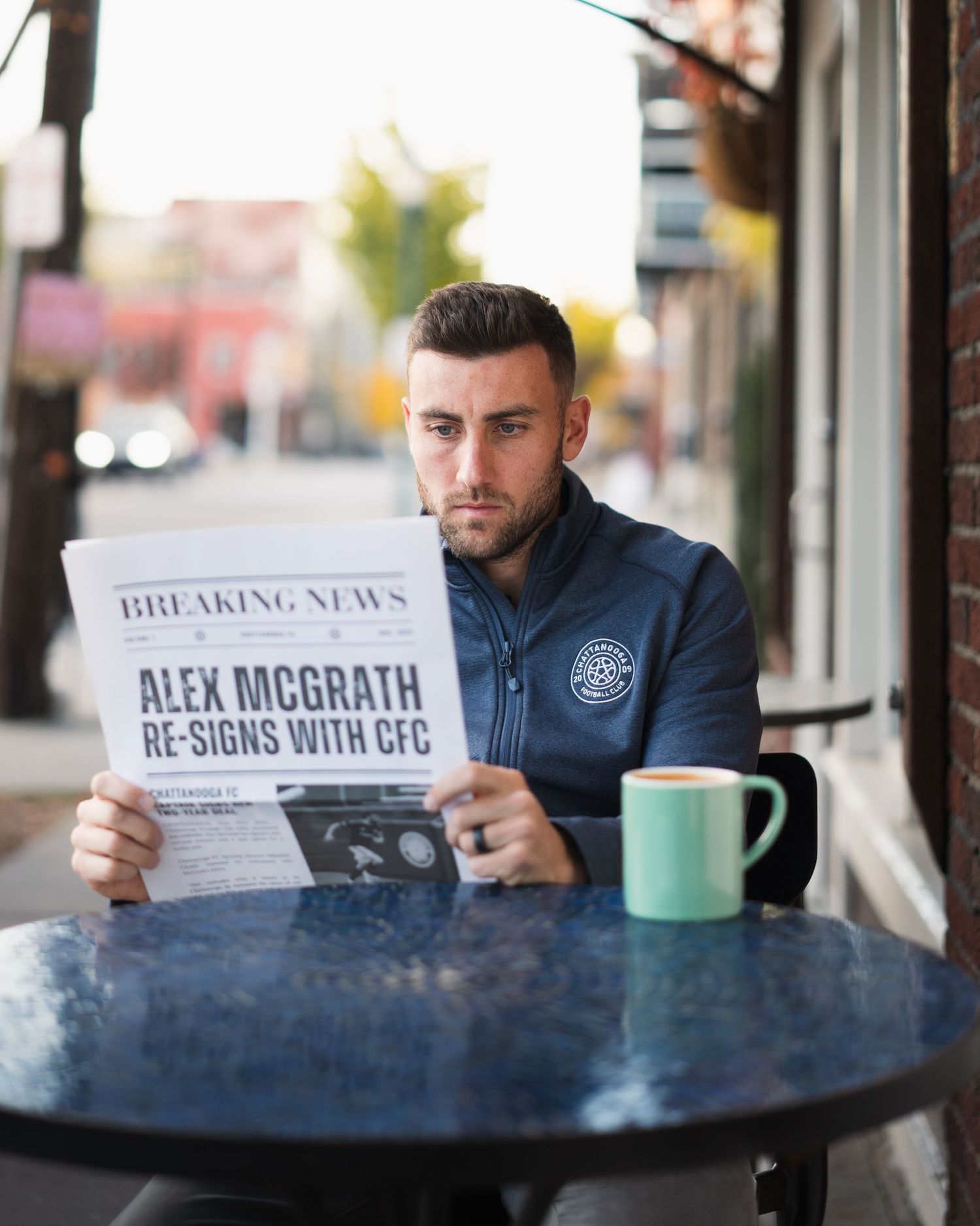 Man reads Breaking News newspaper about Alex McGrath re-signing with CFC at outdoor cafe table. Photographed for player signing.