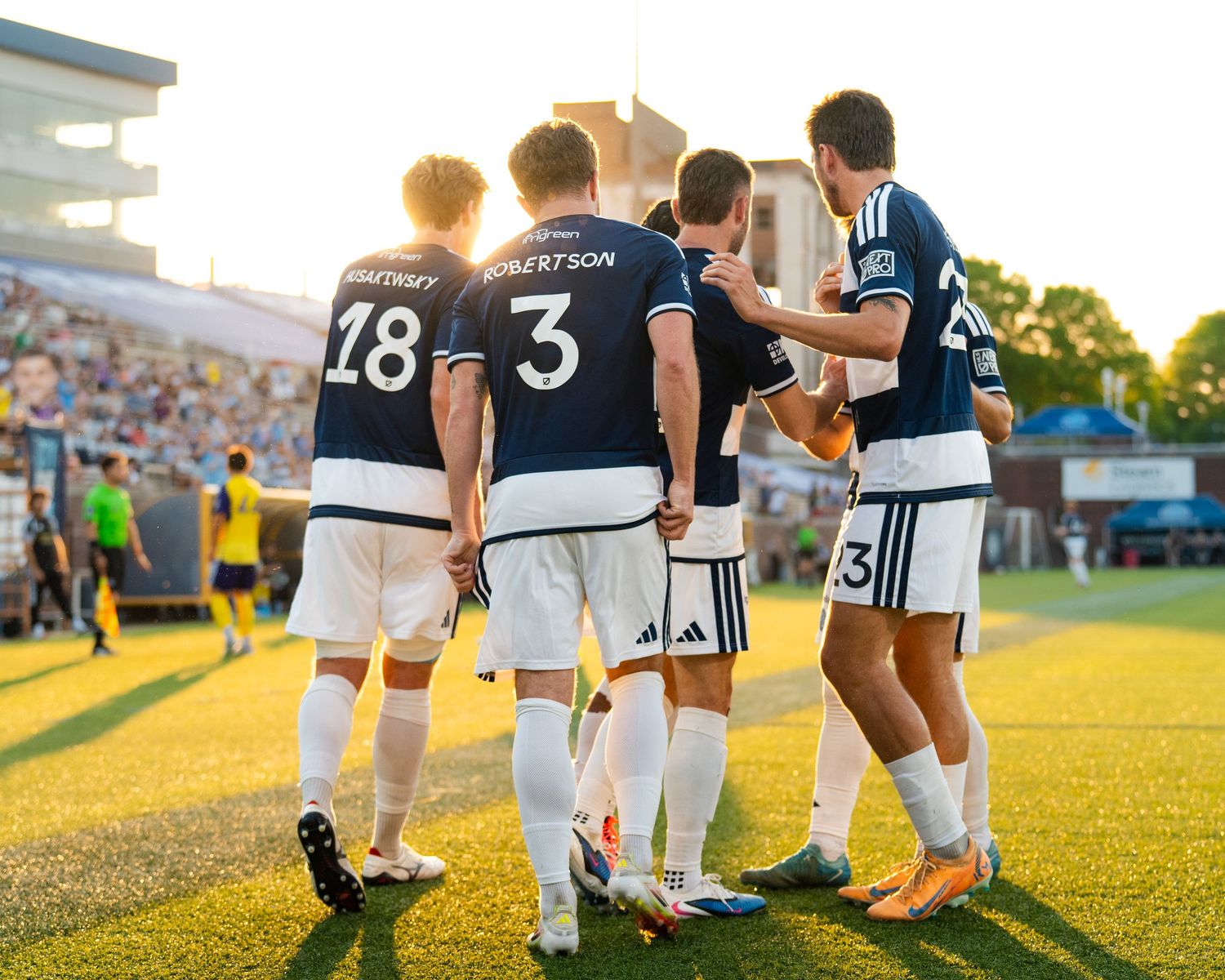 Chattanooga FC Soccer players huddle together celebrating with Robertson number 3 visible on navy blue jersey.