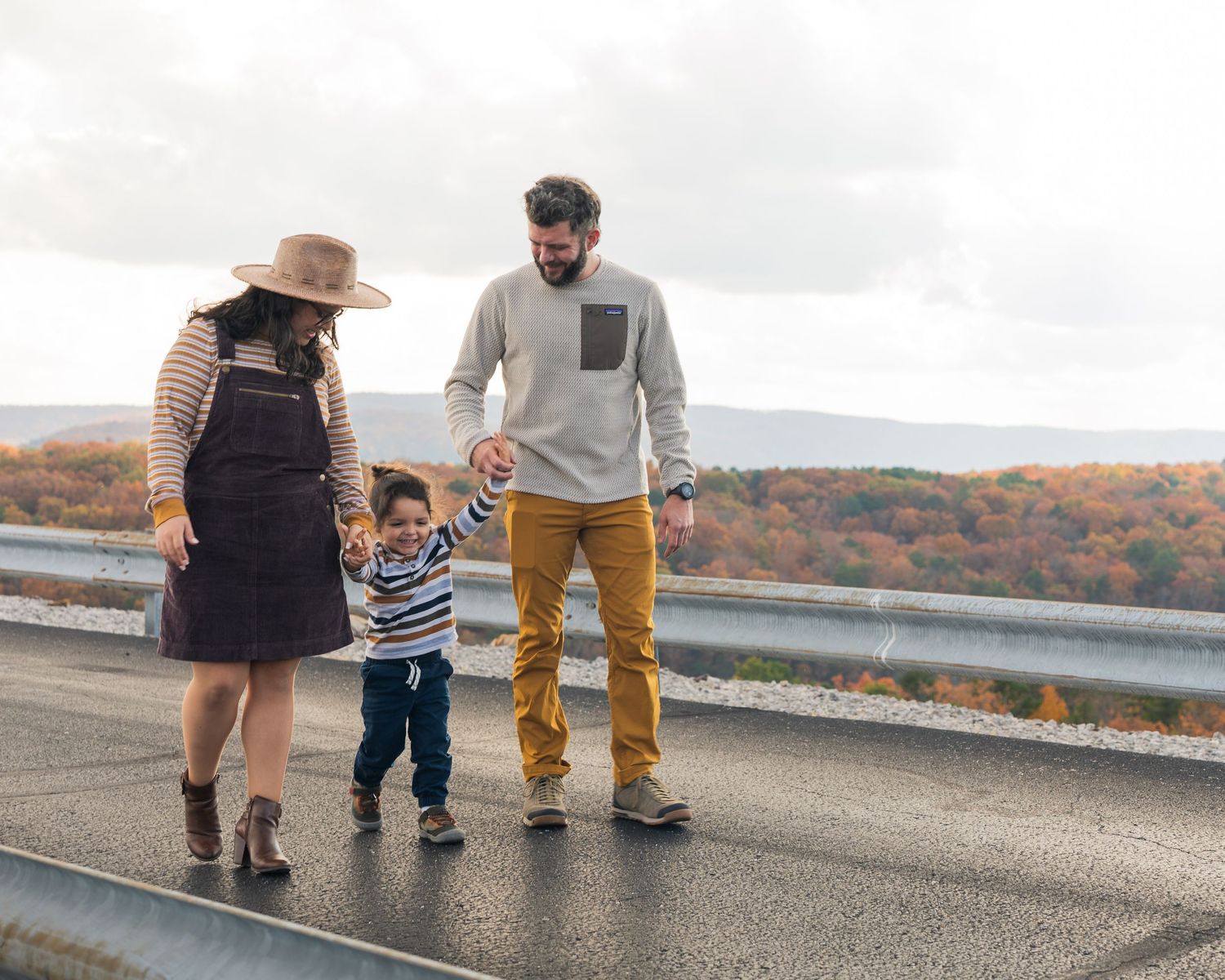 Young family of three walks together on scenic overlook road with colorful autumn foliage background in Chattanooga, TN.