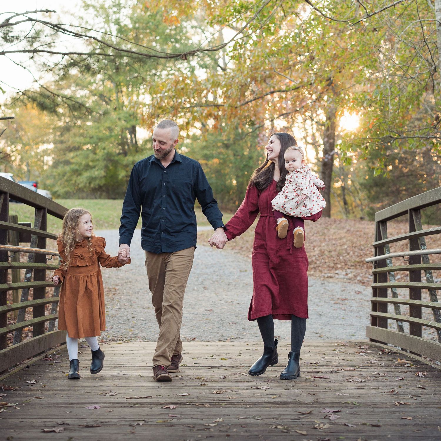 Joyful family walks hand-in-hand across wooden bridge in golden autumn forest in Chattanooga, TN.