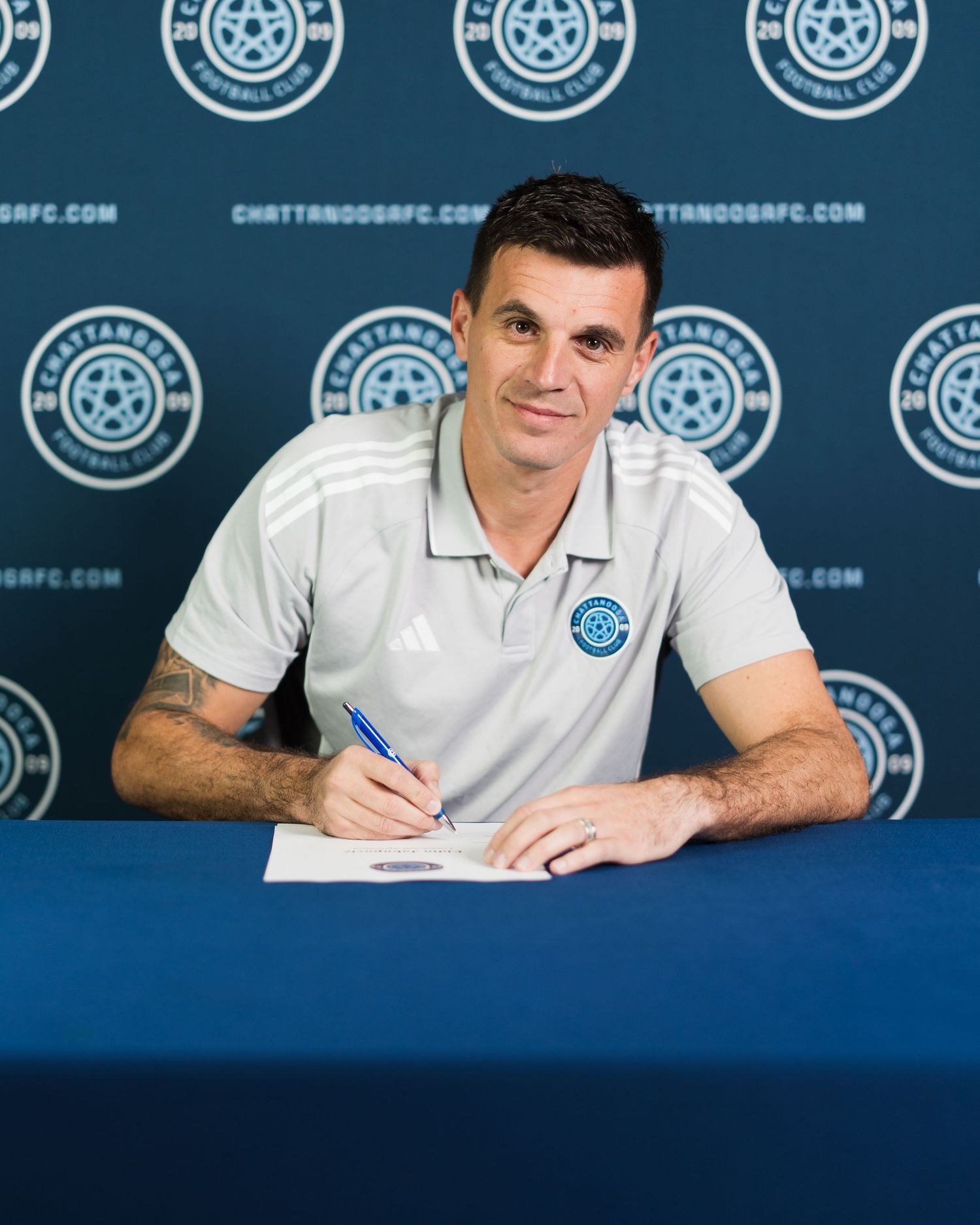 Chattanooga FC player smiles while signing contract at table in front of branded backdrop. Photographed for Chattanooga FC player signing.