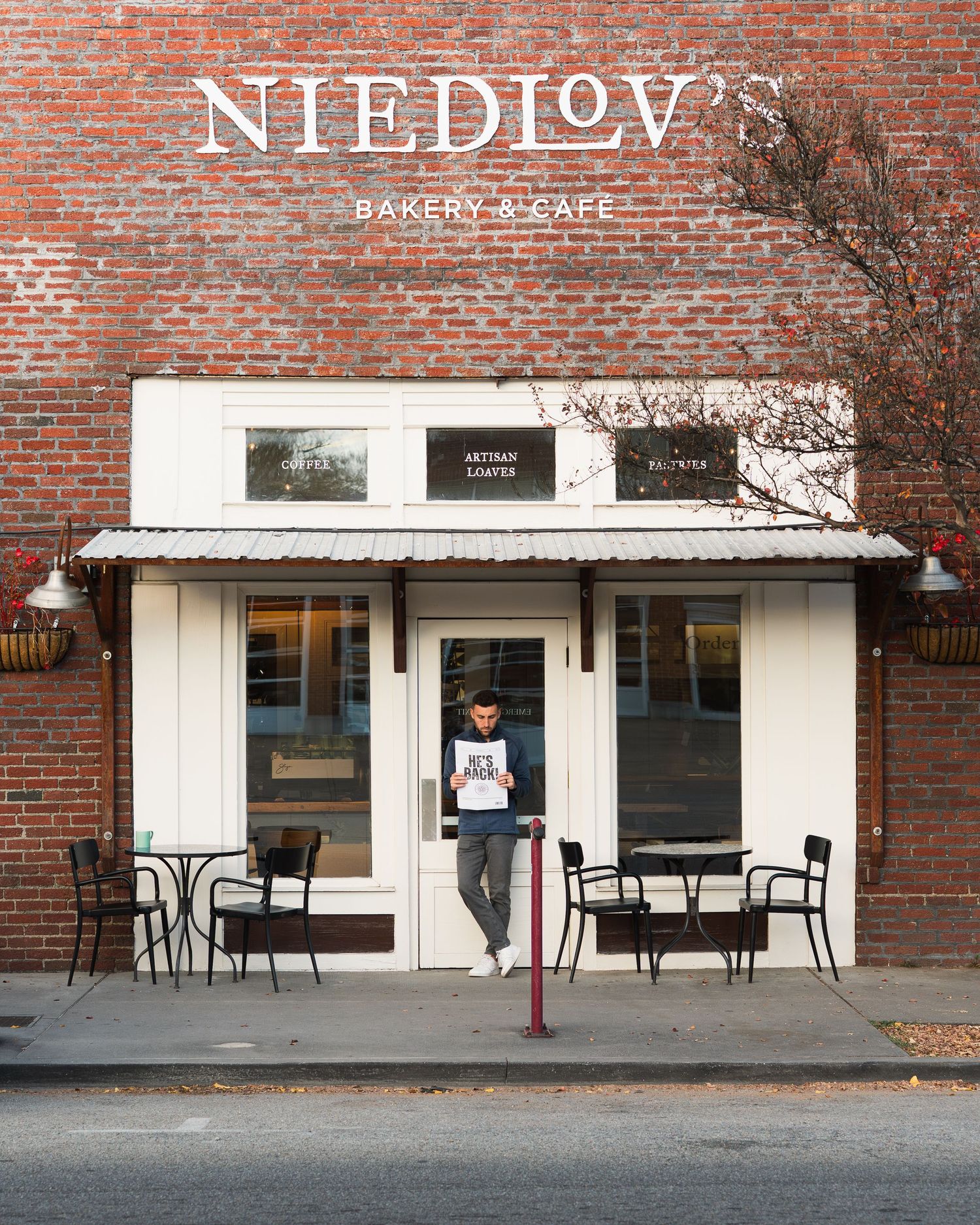 Man stands outside Niedlov's Bakery and Cafe holding newspaper on quiet street. Photographed for Chattanooga FC player signing.