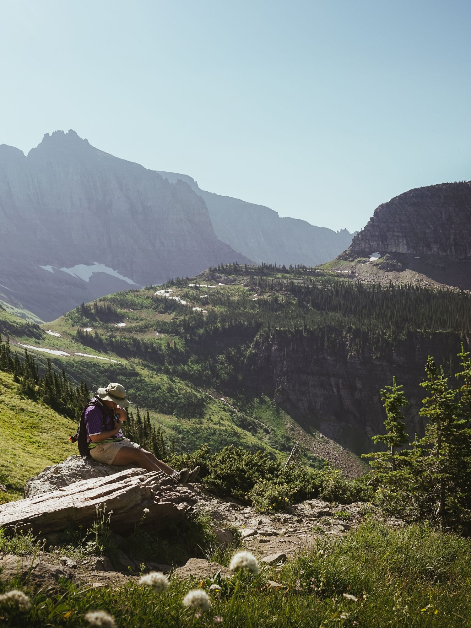 Hiker resting on a rock with panoramic mountain valley views in Glacier National Park.