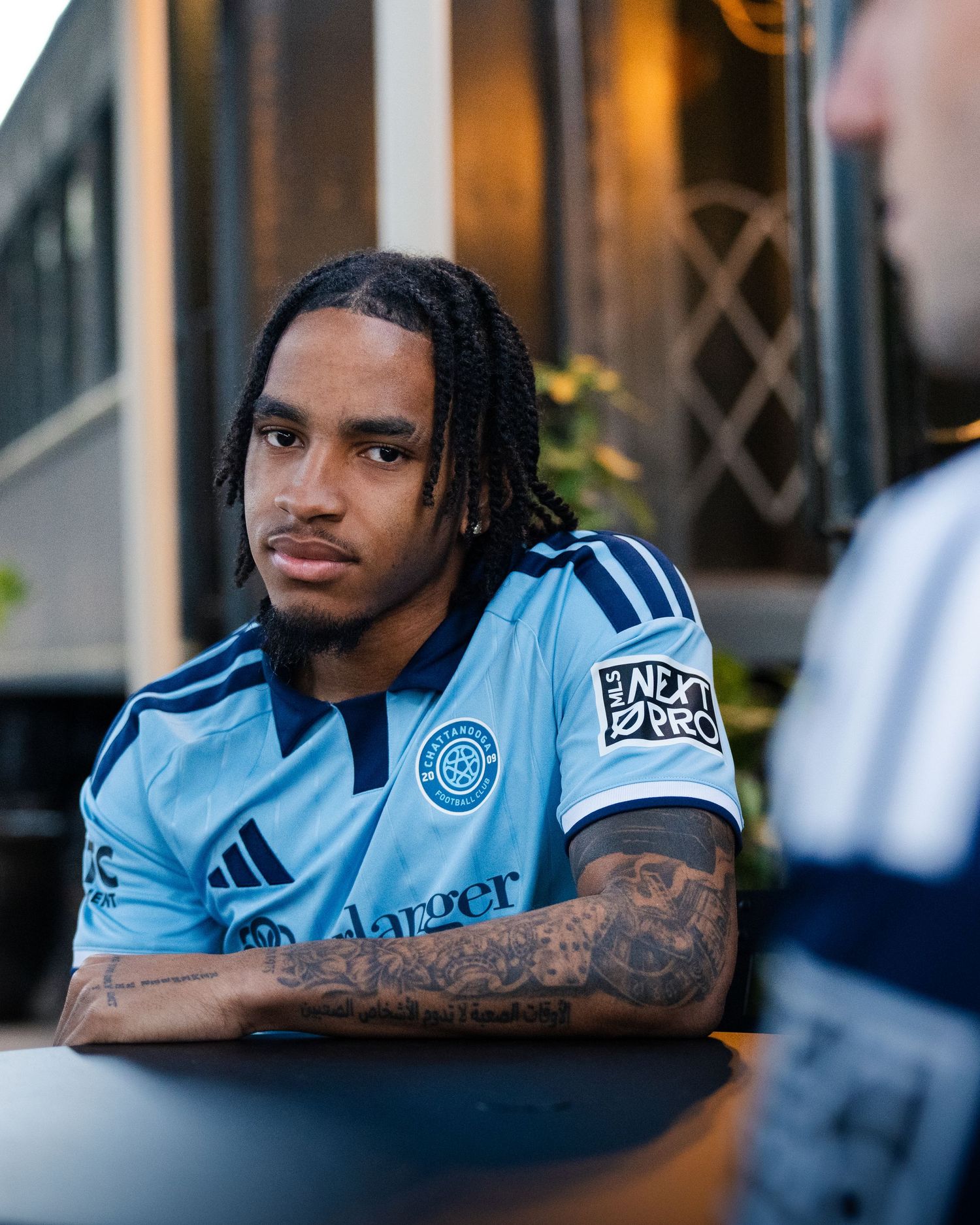 Chattanooga FC player with tattoos wearing light blue jersey sits outdoors photographed for a creative sports assignment in Chattanooga, TN.