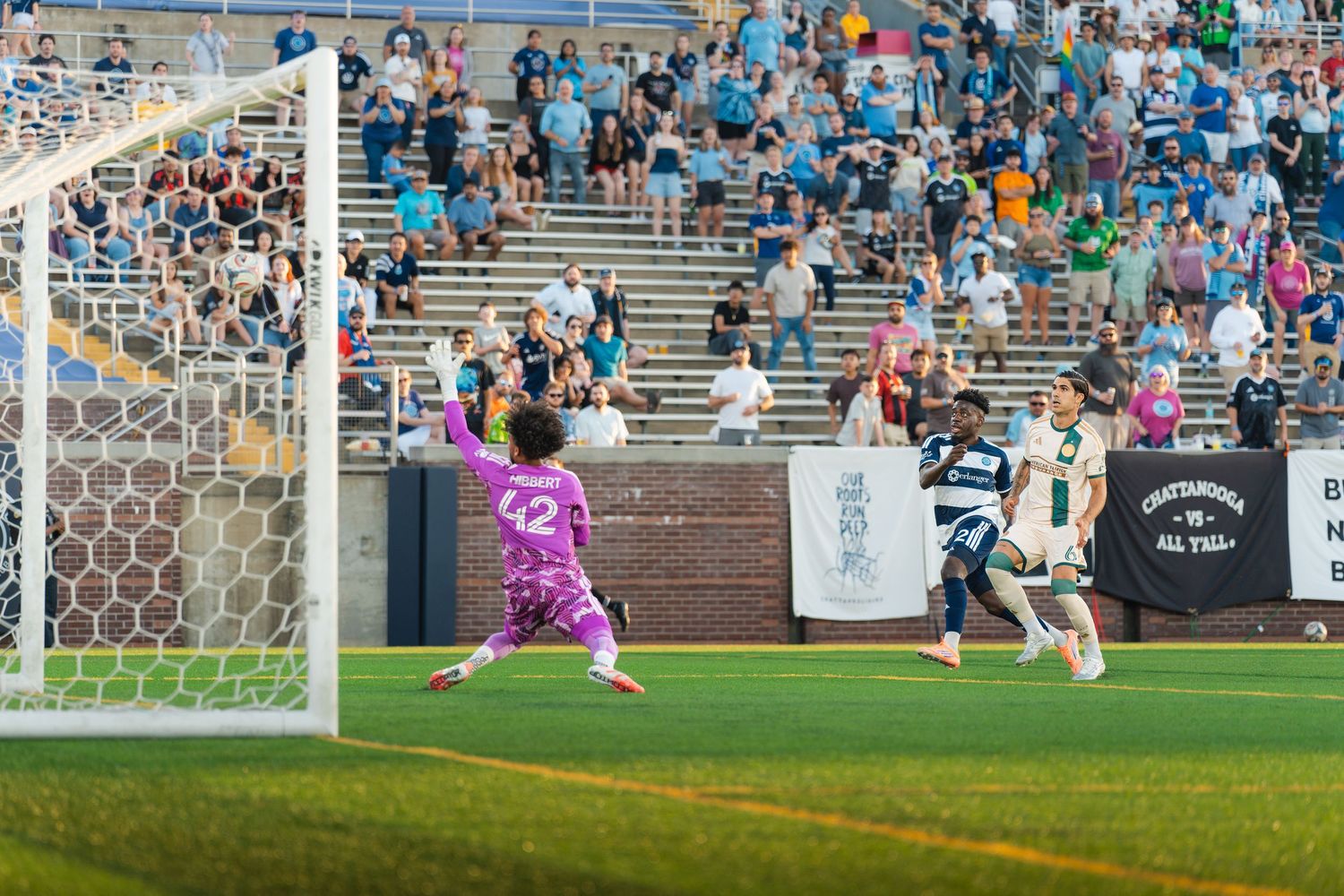 Chattanooga FC Soccer player shoots toward goal as goalkeeper in purple kit prepares to defend during a U.S. Open Cup match.