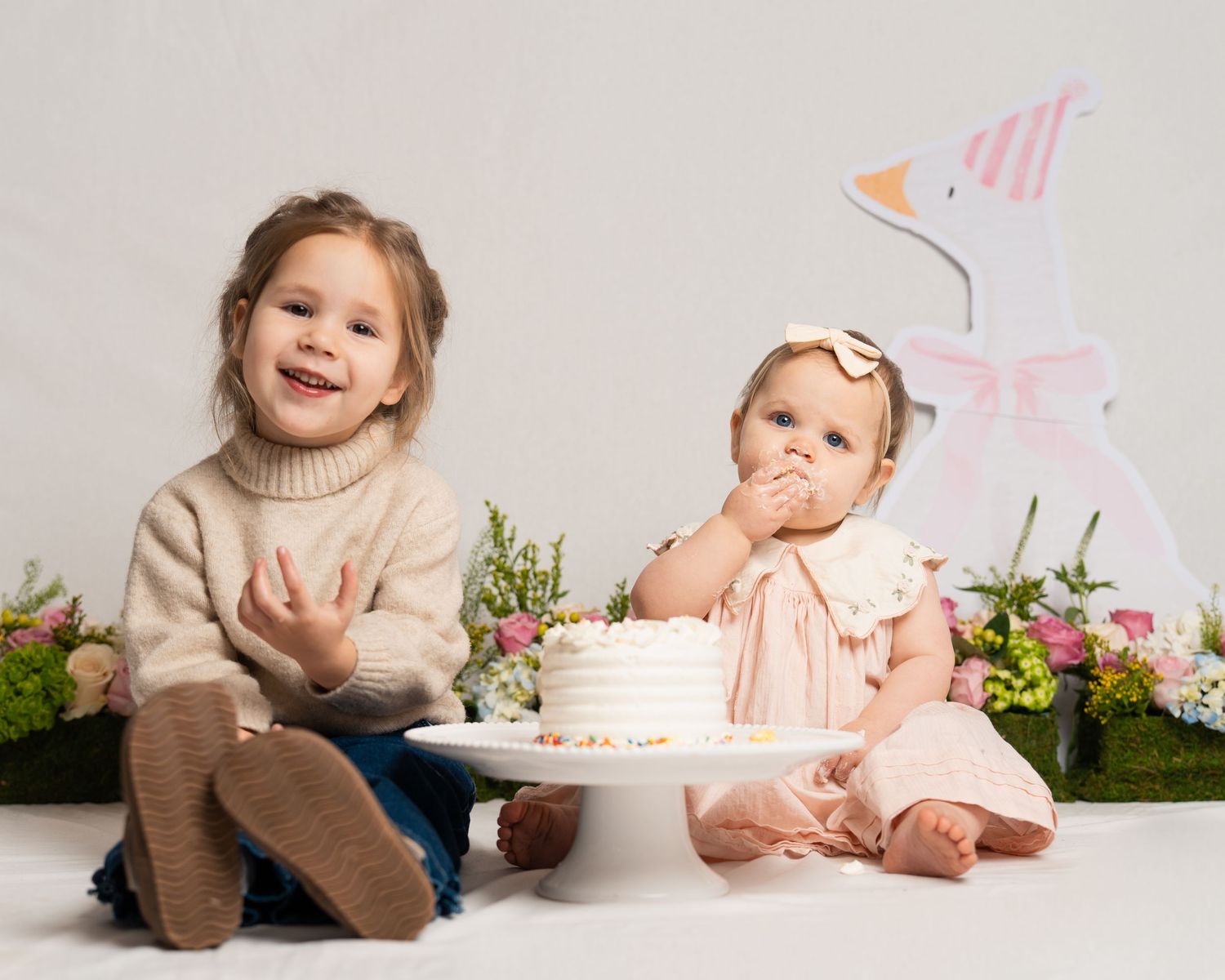Two young sisters celebrating first birthday with white cake and Easter decor.
