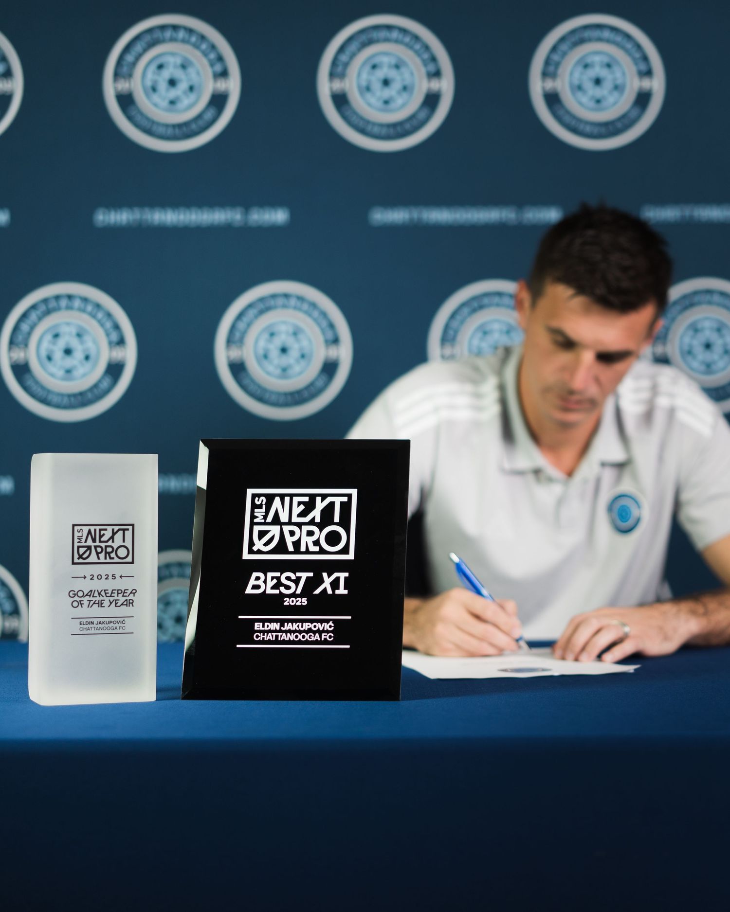 Chattanooga FC player signs contract beside MLS Next Pro Best XI 2024 awards on a table. Photographed for Chattanooga FC player signing.