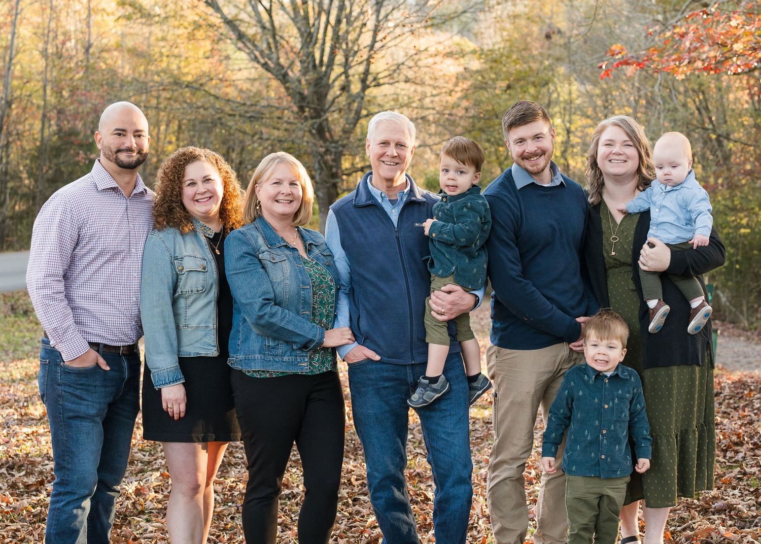 A multigenerational family poses together smiling outdoors among colorful fall foliage in Chattanooga, TN.