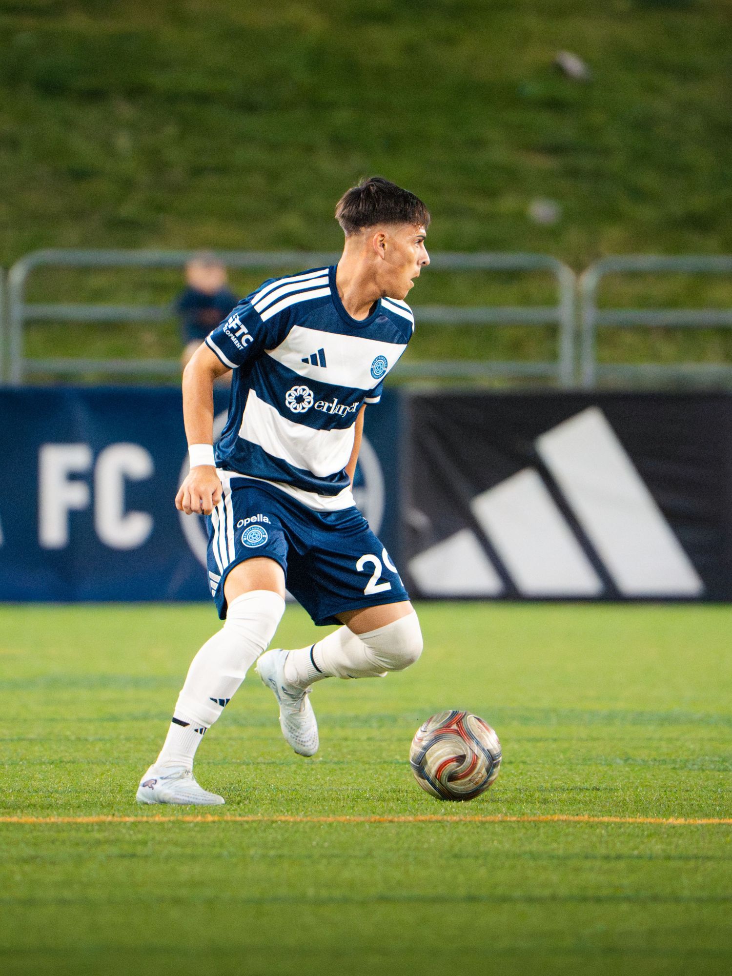 Chattanooga FC Soccer player in blue and white kit dribbles the ball during a nighttime MLS Next Pro match.
