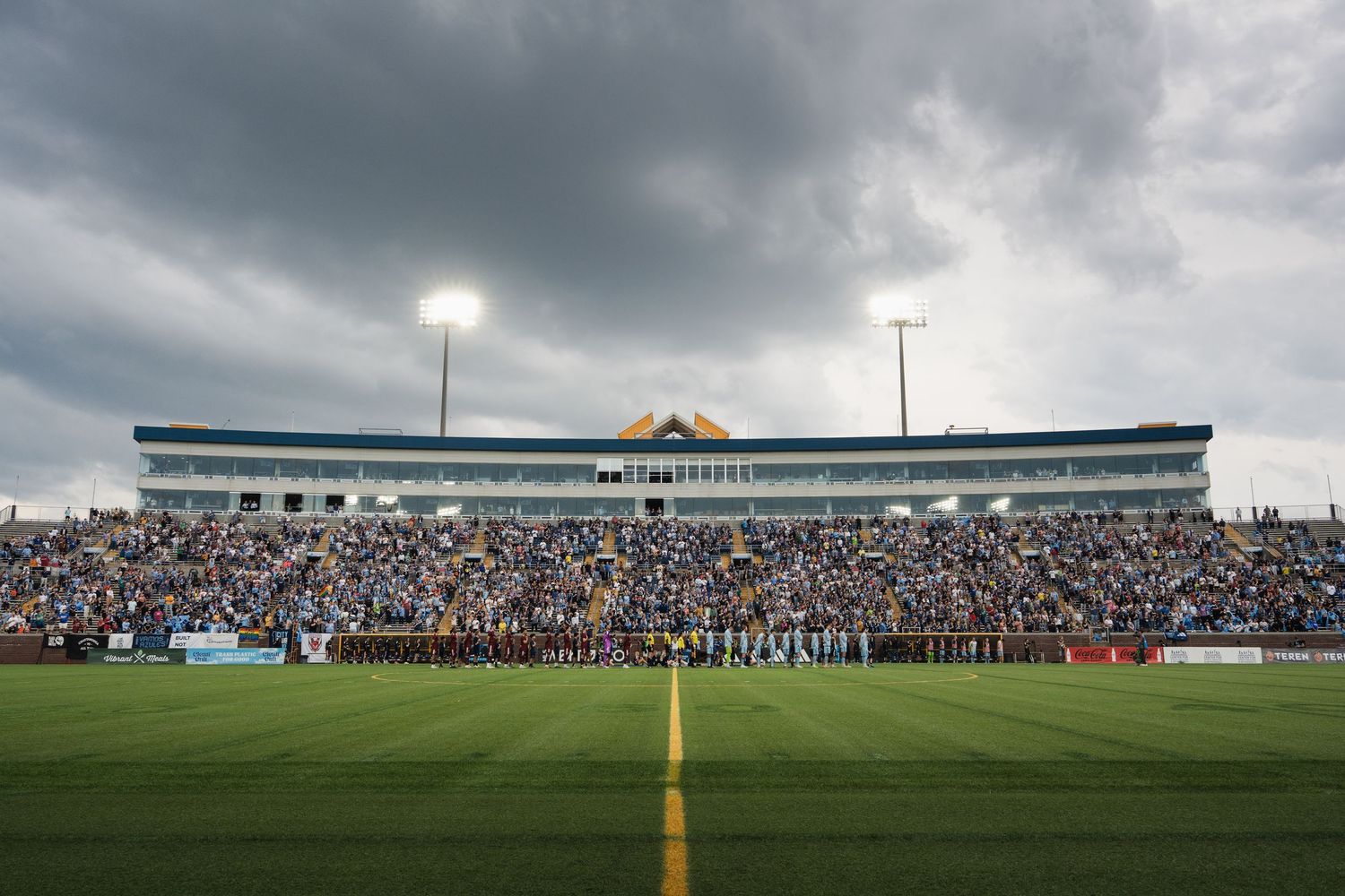 Packed Chattanooga FC soccer stadium with cloudy skies as teams line up on field before match.