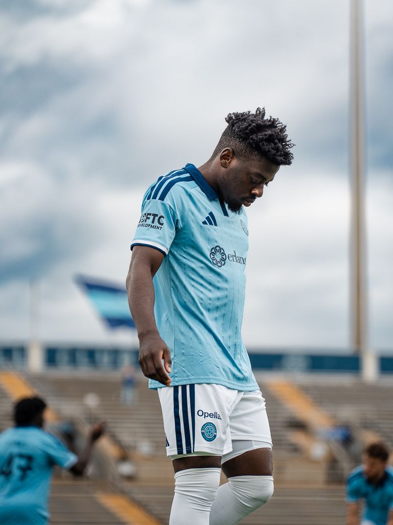 Chattanooga FC Soccer player in light blue Adidas kit looks down on the field during a cloudy match day.