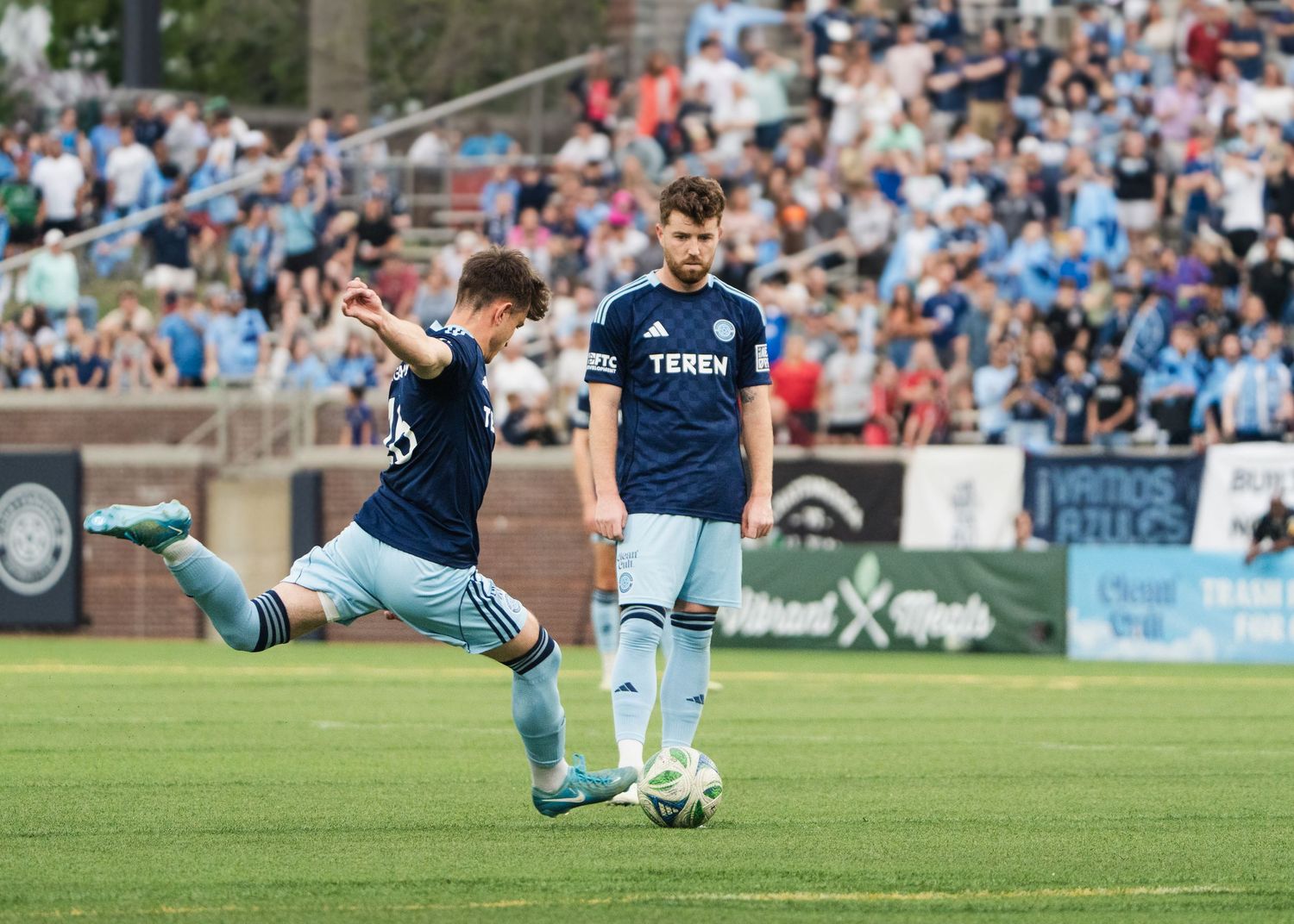 Chattanooga FC Soccer player takes powerful shot during competitive match with crowd in background.