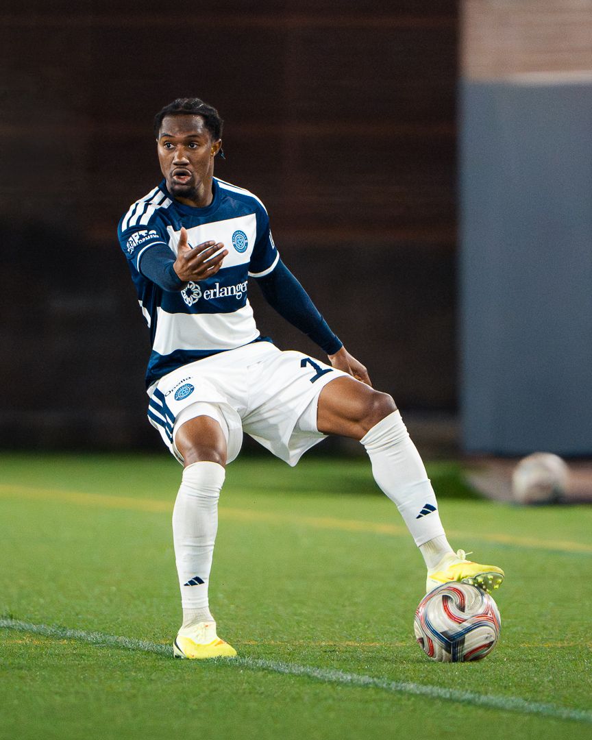 Chattanooga FC Soccer player in navy blue Erlanger-sponsored jersey controls the ball on a green turf field.